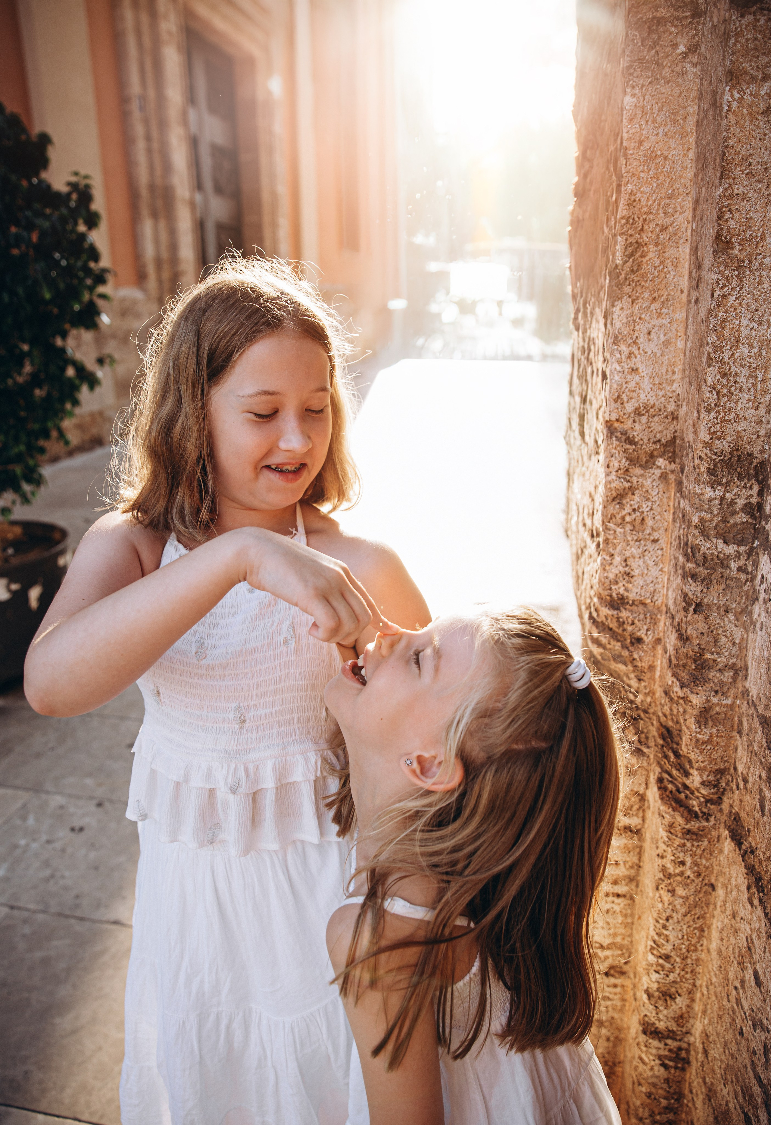 Dos hermanas comparten un dulce momento de juego bajo la luz dorada del sol durante una sesión familiar en Valencia, España — capturando la alegría infantil espontánea en el corazón de la ciudad vieja. Ideal para quienes buscan sesiones cálidas y naturales en Valencia y toda España.
