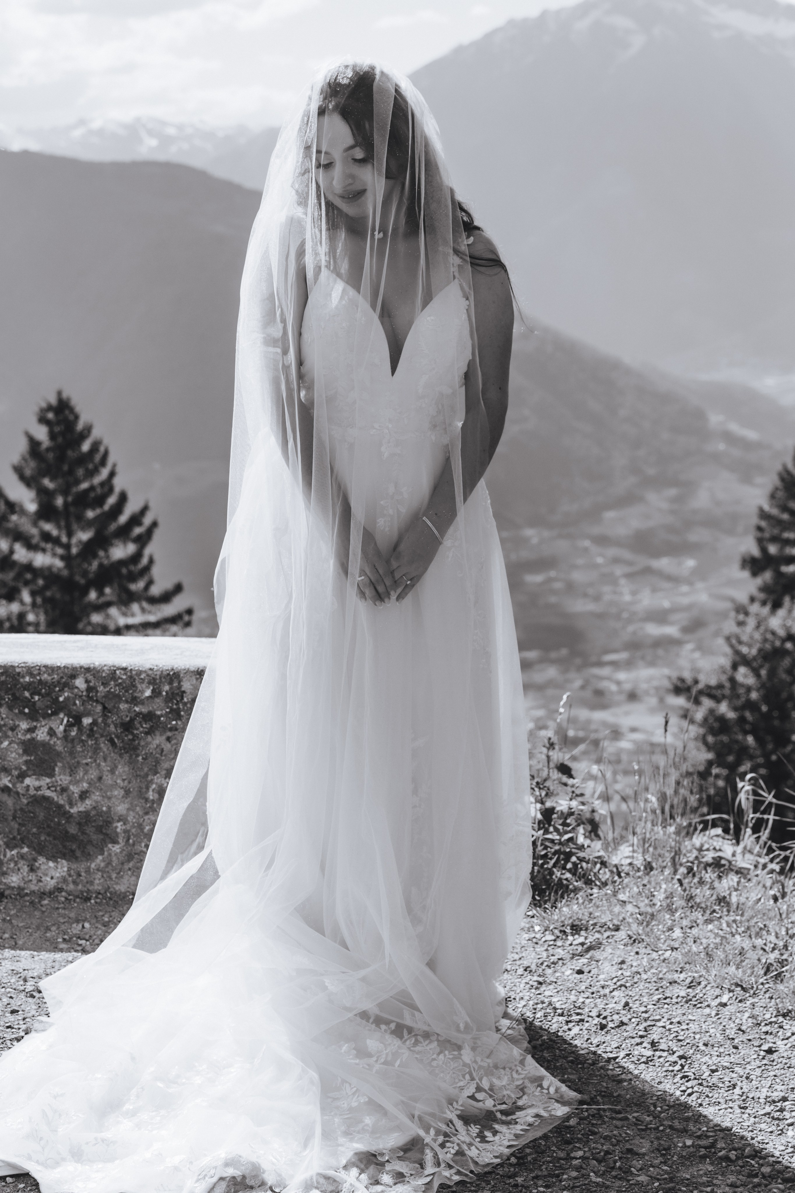 Die Braut steht vor einer atemberaubenden Bergkulisse, ihr Gesicht zart von einem Schleier bedeckt.
