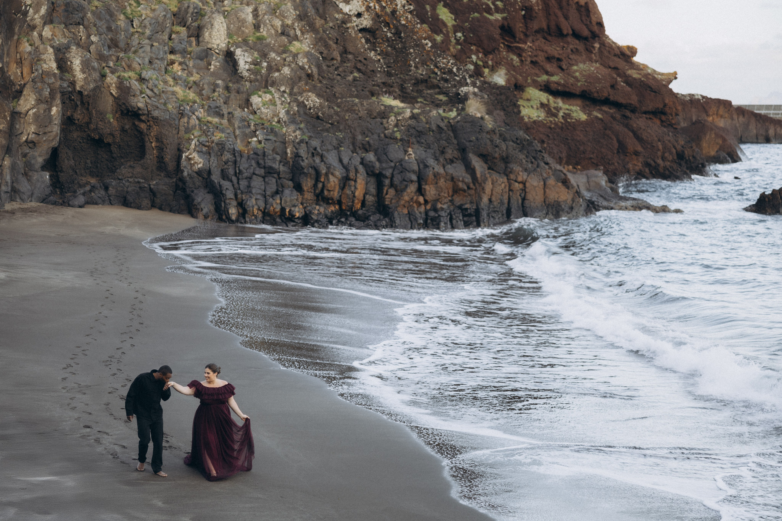 A glowing expectant mother standing on a cliff overlooking the ocean in Madeira, her dress flowing gently in the wind as the golden sunset casts a warm glow.