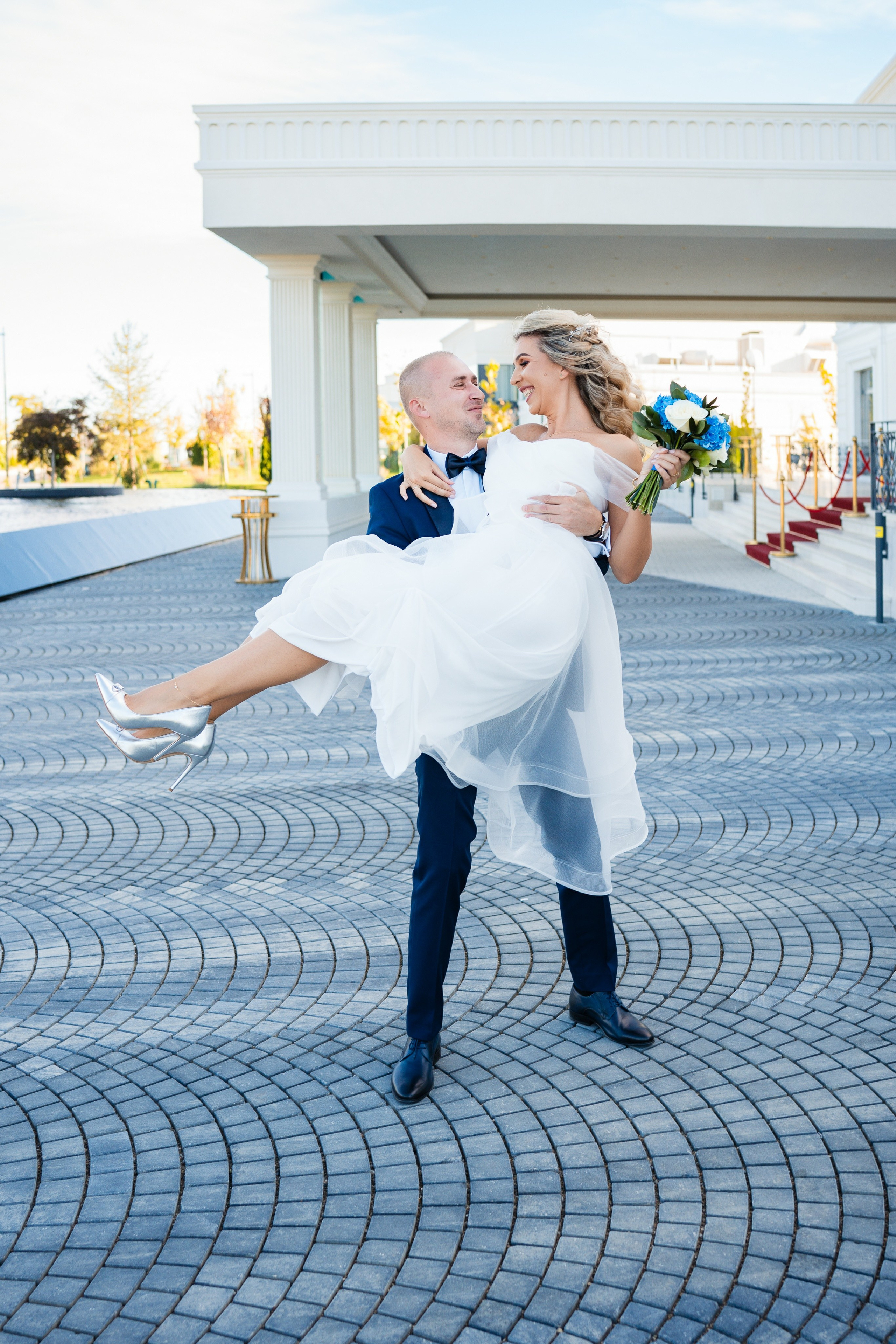 Mireasa râzând în brațele mirelui, într-un peisaj de poveste