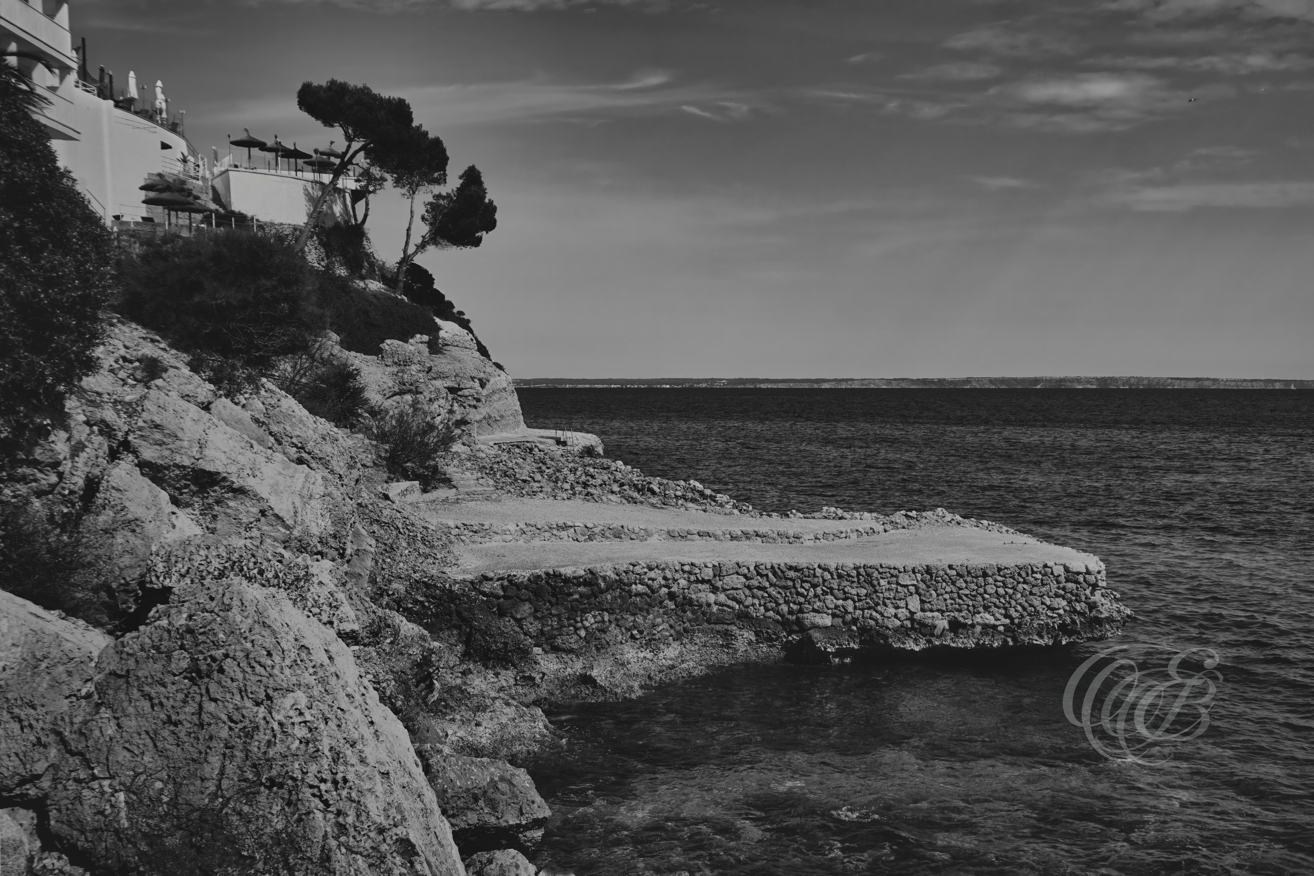 The Torrenova cliffs near Magaluf overlook one of Mallorca’s most recognizable coastal regions, where limestone formations have long shaped the appearance of the shoreline. In this black and white matte presentation, attention shifts toward the natural patterns, tonal variations, and visual structure of the landscape. The restrained palette enhances the relationship between land and sea, offering a contemplative view of Mallorca’s coastal environment. Eduardo Bartoli Photography.