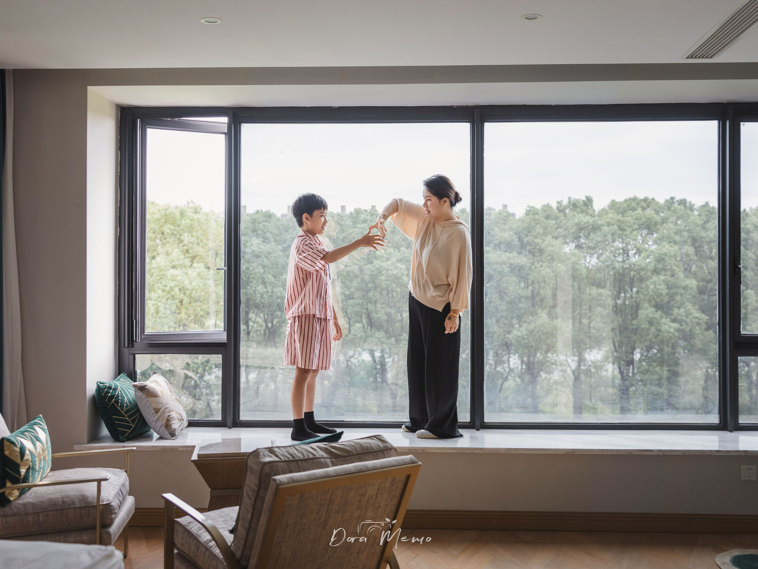 Mother and son stand by a large window in their home during a natural family photography session.