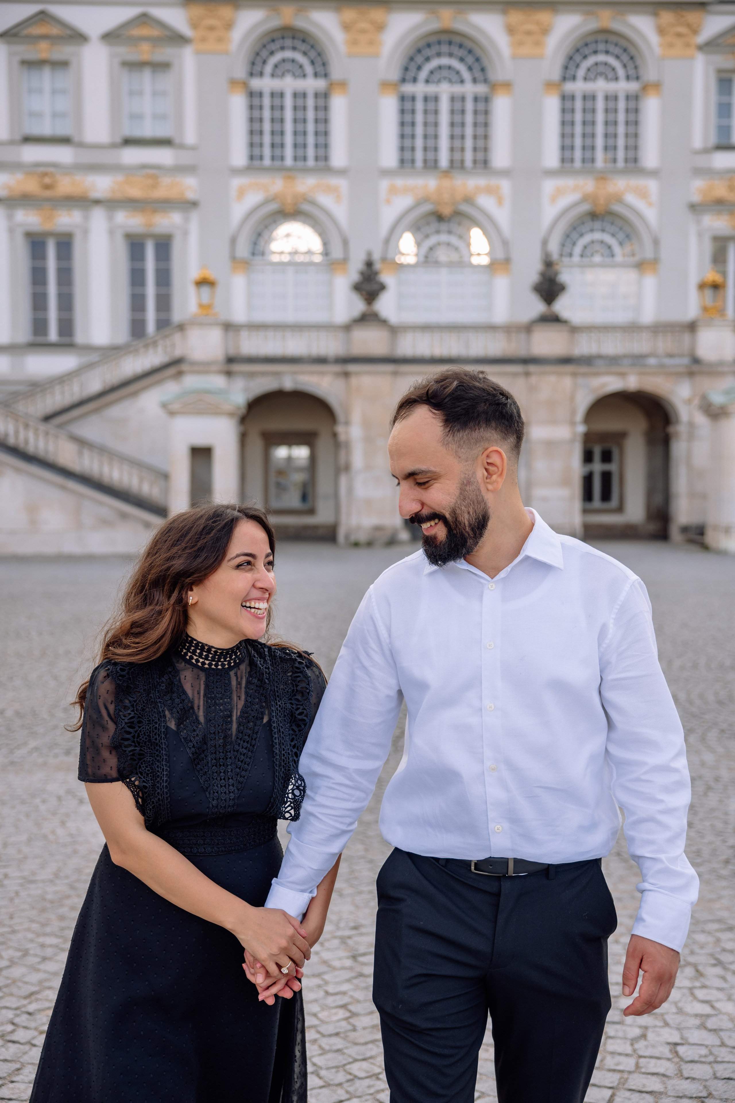 Verlobtes Paar läuft Hand in Hand lachend vor dem Schloss Nymphenburg