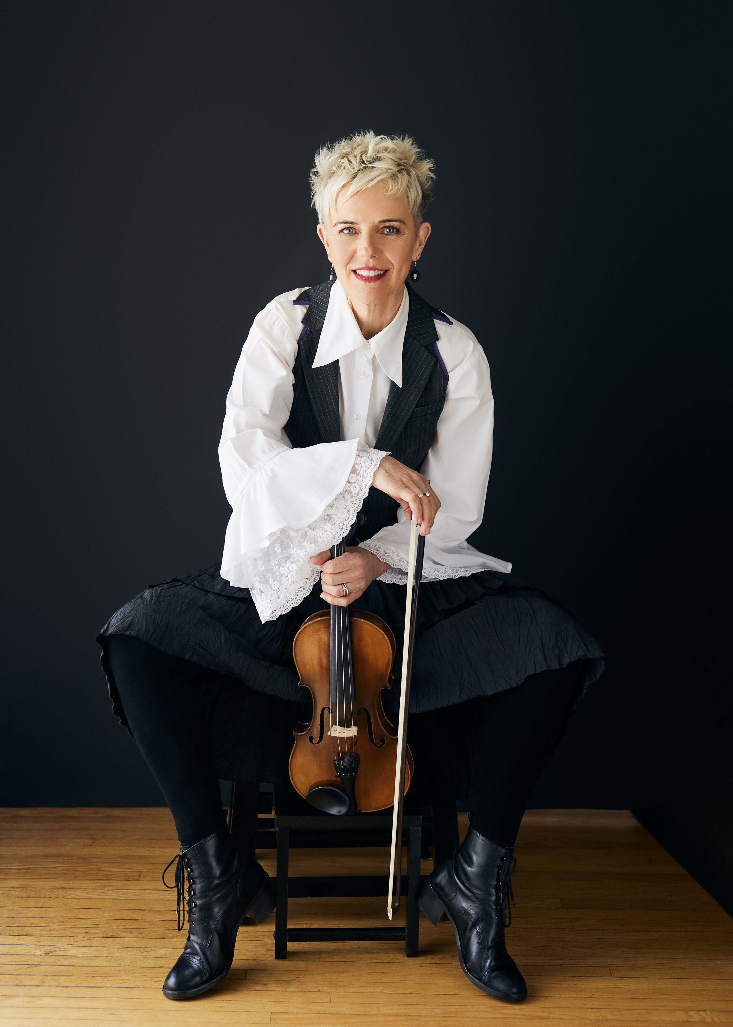 mature woman with short pixie hair cut, wearing ruffled white shirt and holding a violin 