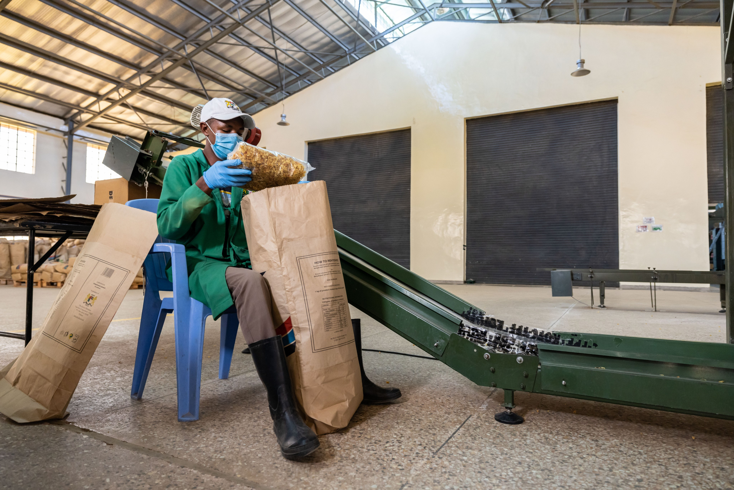 A full shot of a factory worker next to a conveyor belt, packing food in a brown bag, in KOFC, Nakuru. Documentary photography
