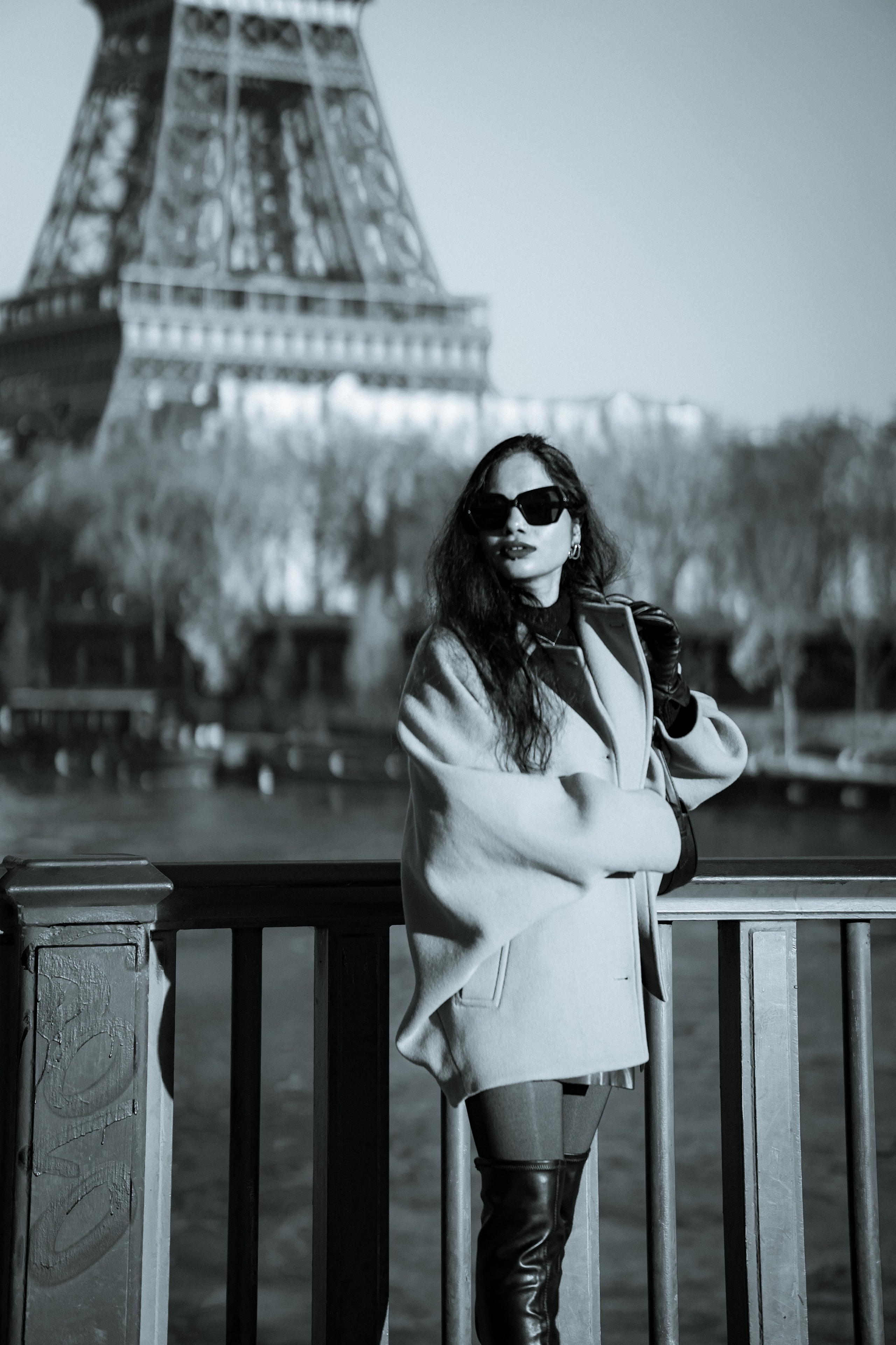 a woman wearing oversized brown jacket and standing with paris bridge and eiffel tower view behind her