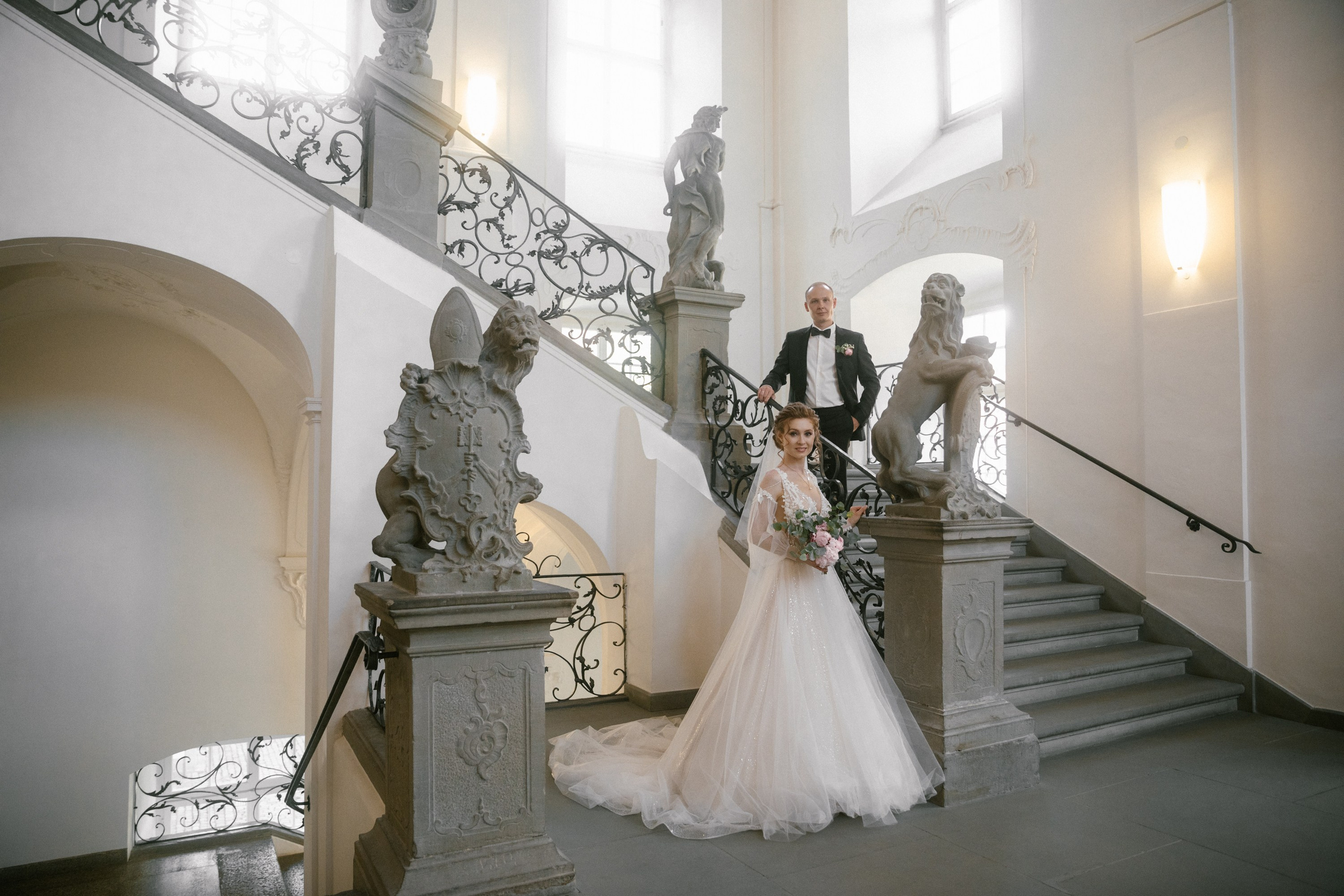 Weitwinkelaufnahme vom Brautpaar auf großer Treppe mit Statuen – im Schloss Meersburg