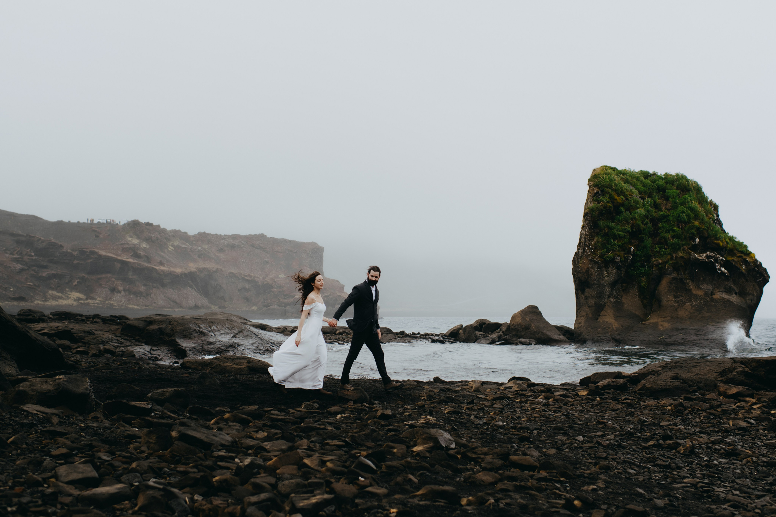 Groom wrapping his arms around the bride as they stand on the rocky edge of Kleifarvatn, braving the cold Icelandic wind.