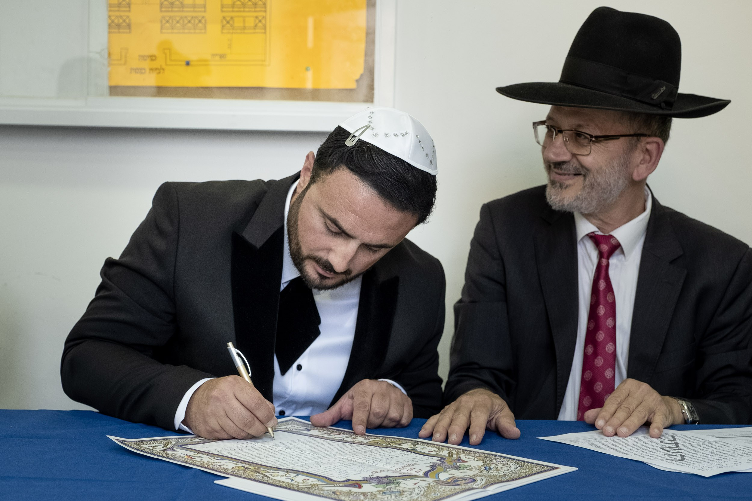 Emil signs the ketubah beside the smiling rabbi