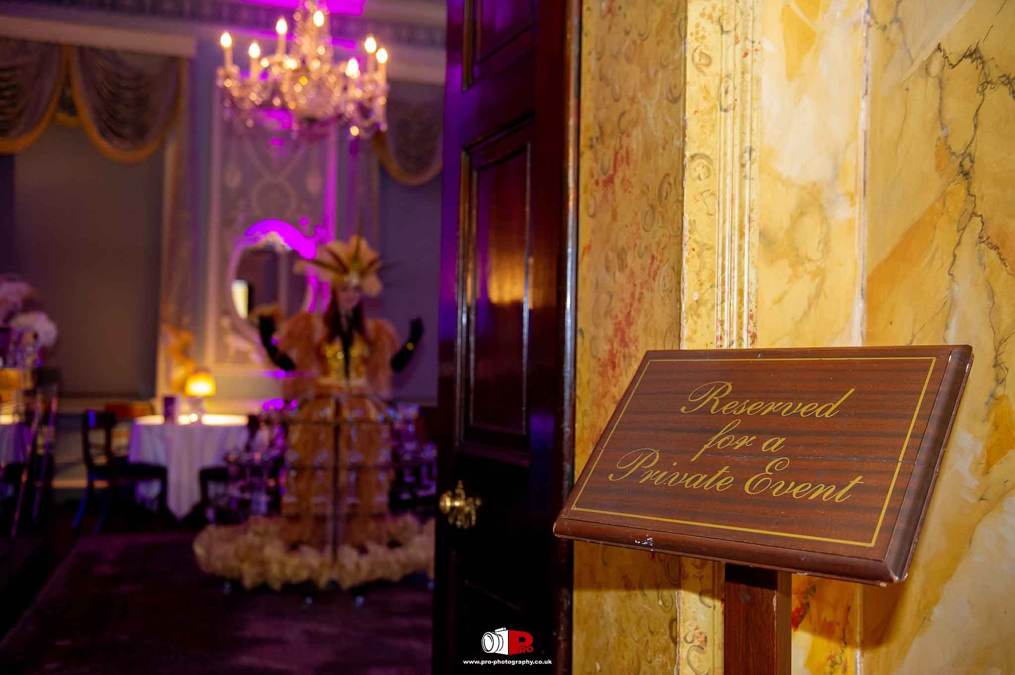 "Reserved for a Private Event" sign with a background of a performer in a golden costume and feathered wings in a luxurious room.