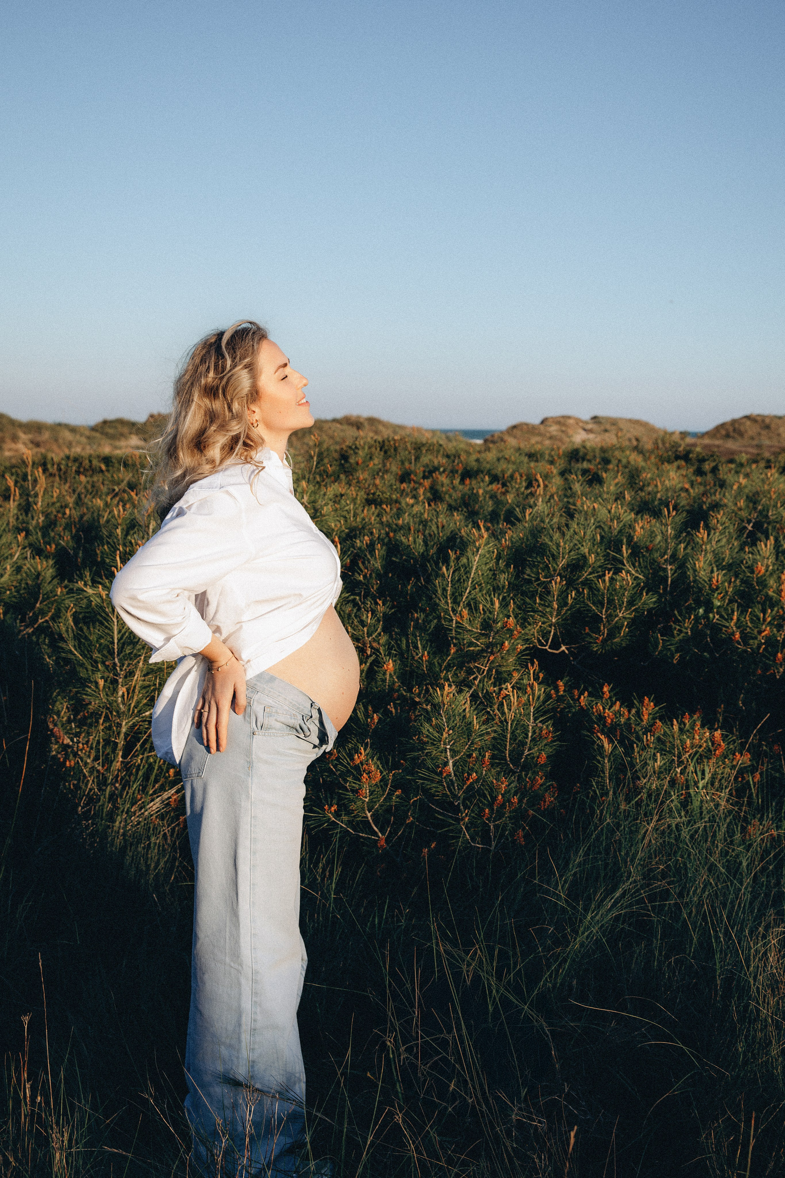 Sesión de fotos de embarazo en Valencia, España, con una mujer embarazada caminando por un campo natural al atardecer, capturada con suave luz dorada para una tranquila escena lifestyle y cinematográfica — ideal para sesiones maternity al aire libre en Valencia y España.
