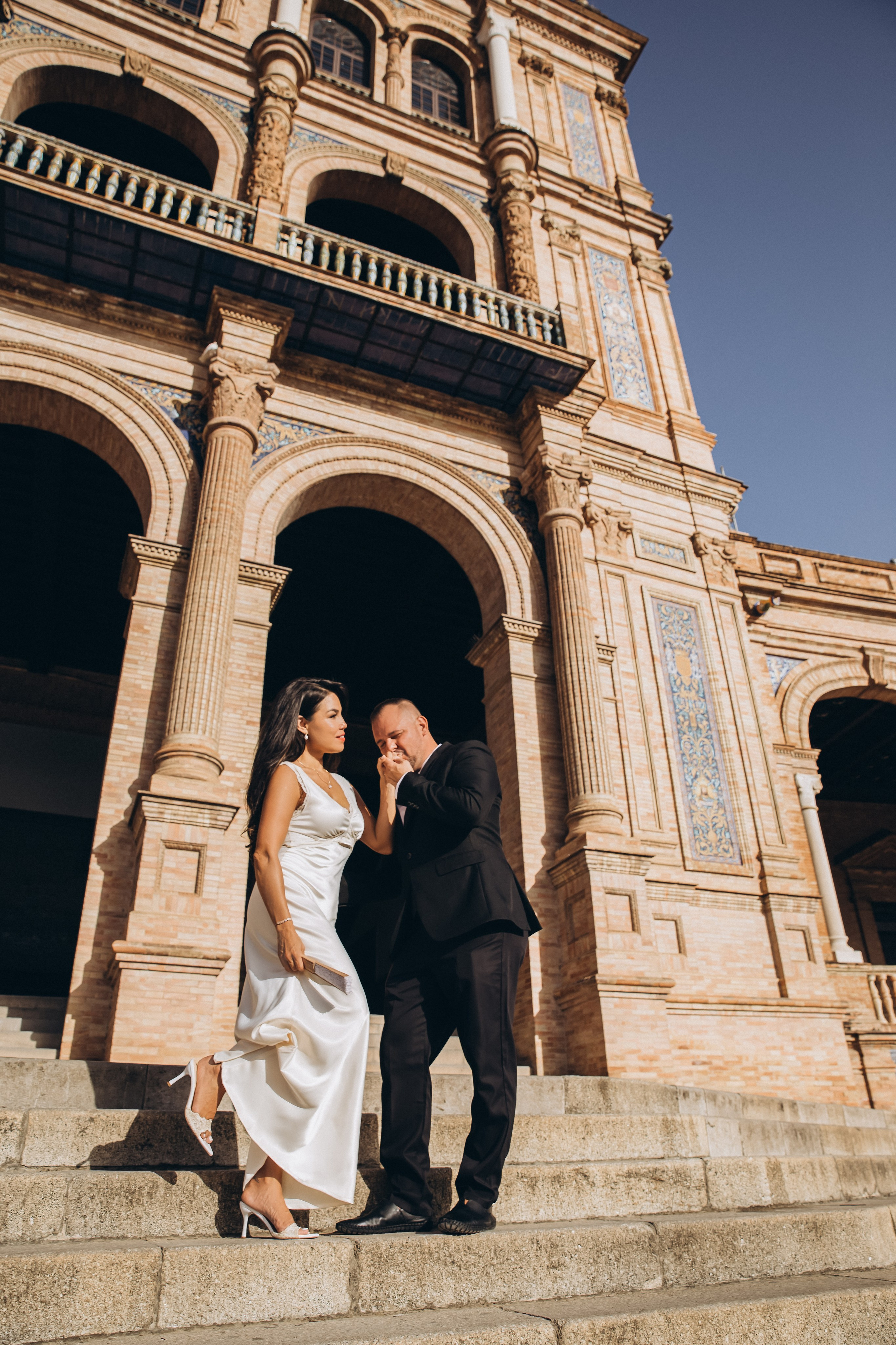 Elegant wedding photoshoot in Valencia, Spain — groom kisses the bride’s hand as they descend a grand stone staircase in front of stunning historic architecture. A romantic and timeless portrait perfect for couples looking for luxury wedding photography in Valencia and iconic Spanish landmarks.
