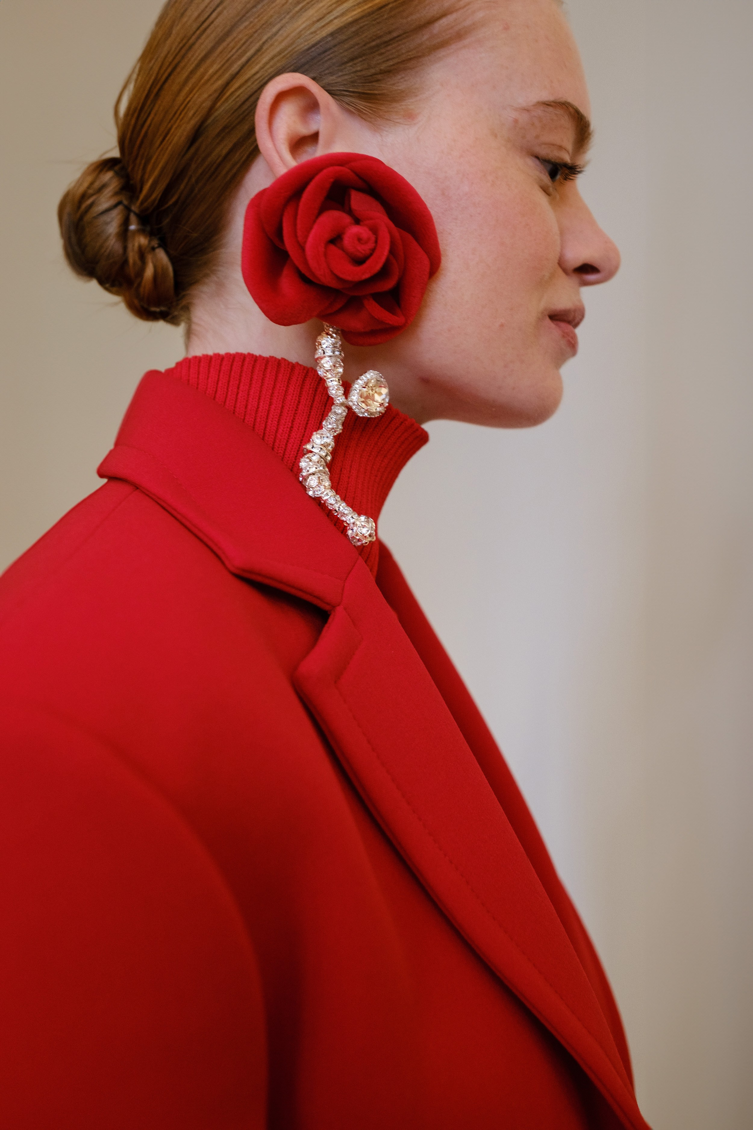 High-end fashion accessory campaign highlighting a statement red rose earring and red coat