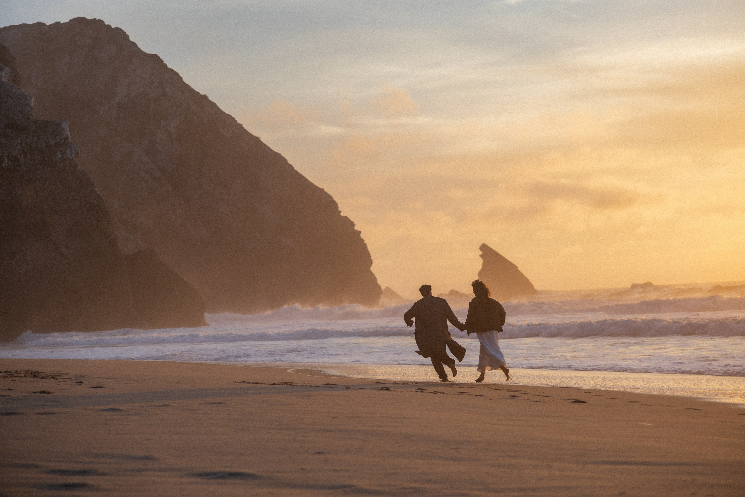 Couple holding hands and walking through a picturesque coastline in Portugal.