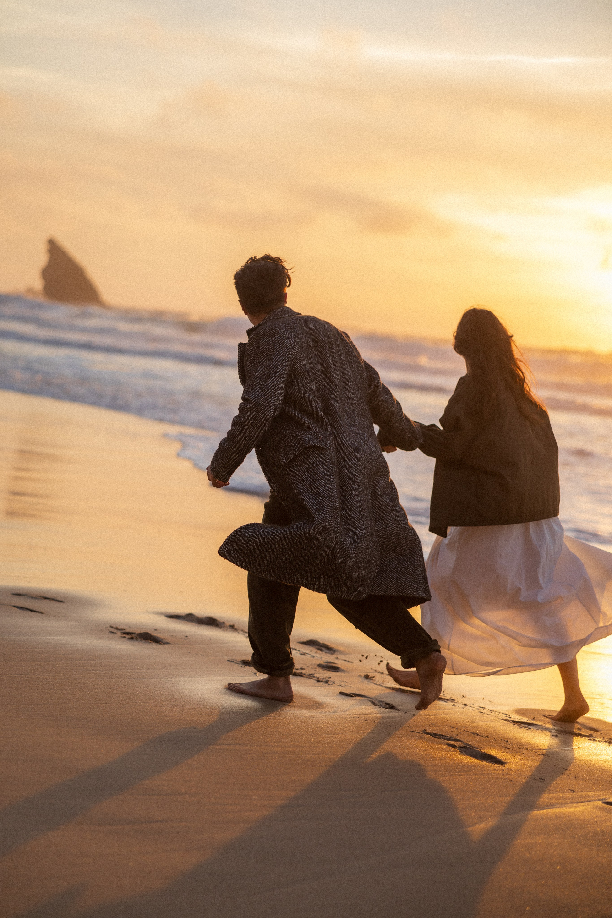 Couple holding hands and walking through a picturesque coastline in Portugal.