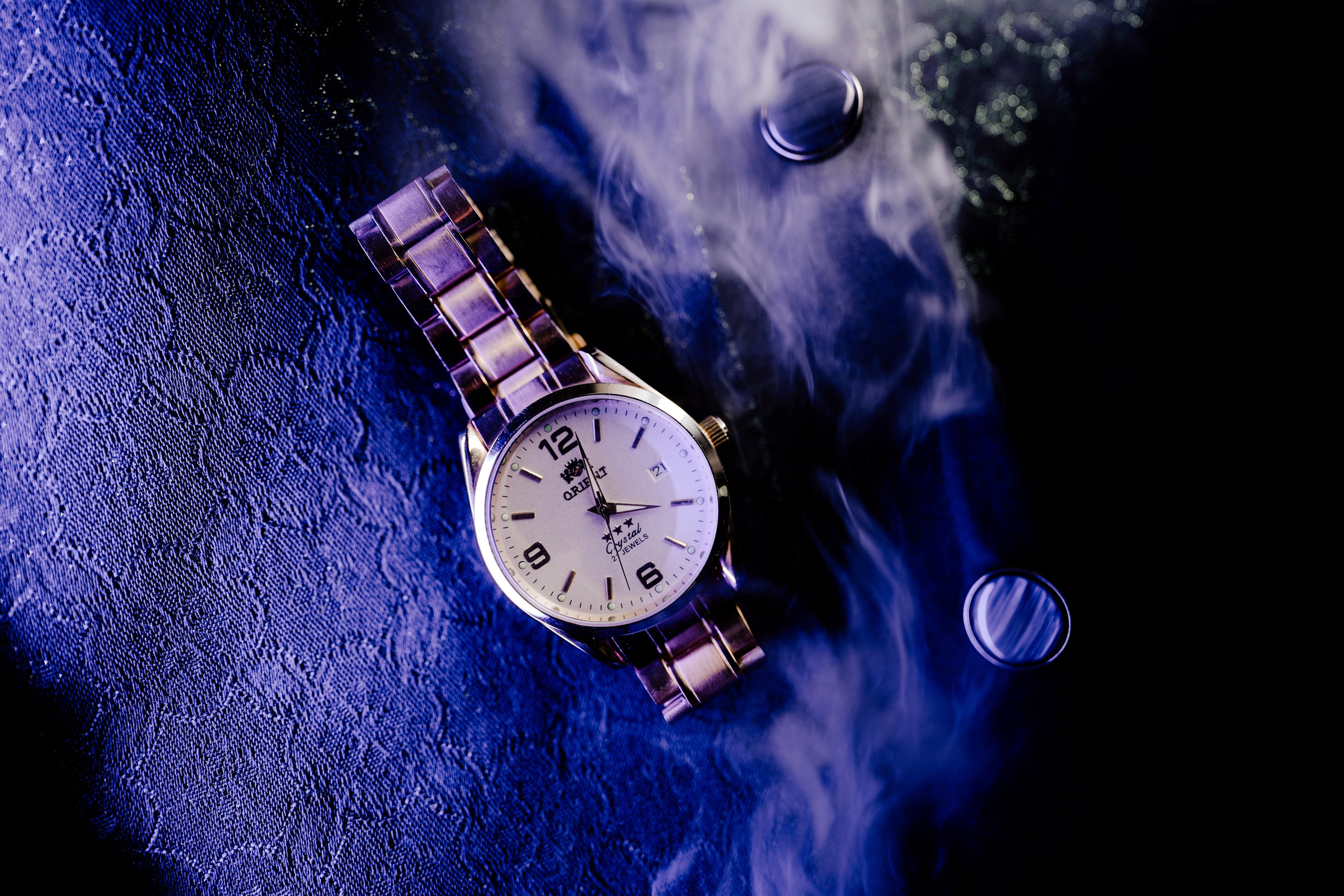 close-up product photo of a gold-tone vintage Orient Crystal 3 Star automatic watch with a white dial on a smoky blue and black background