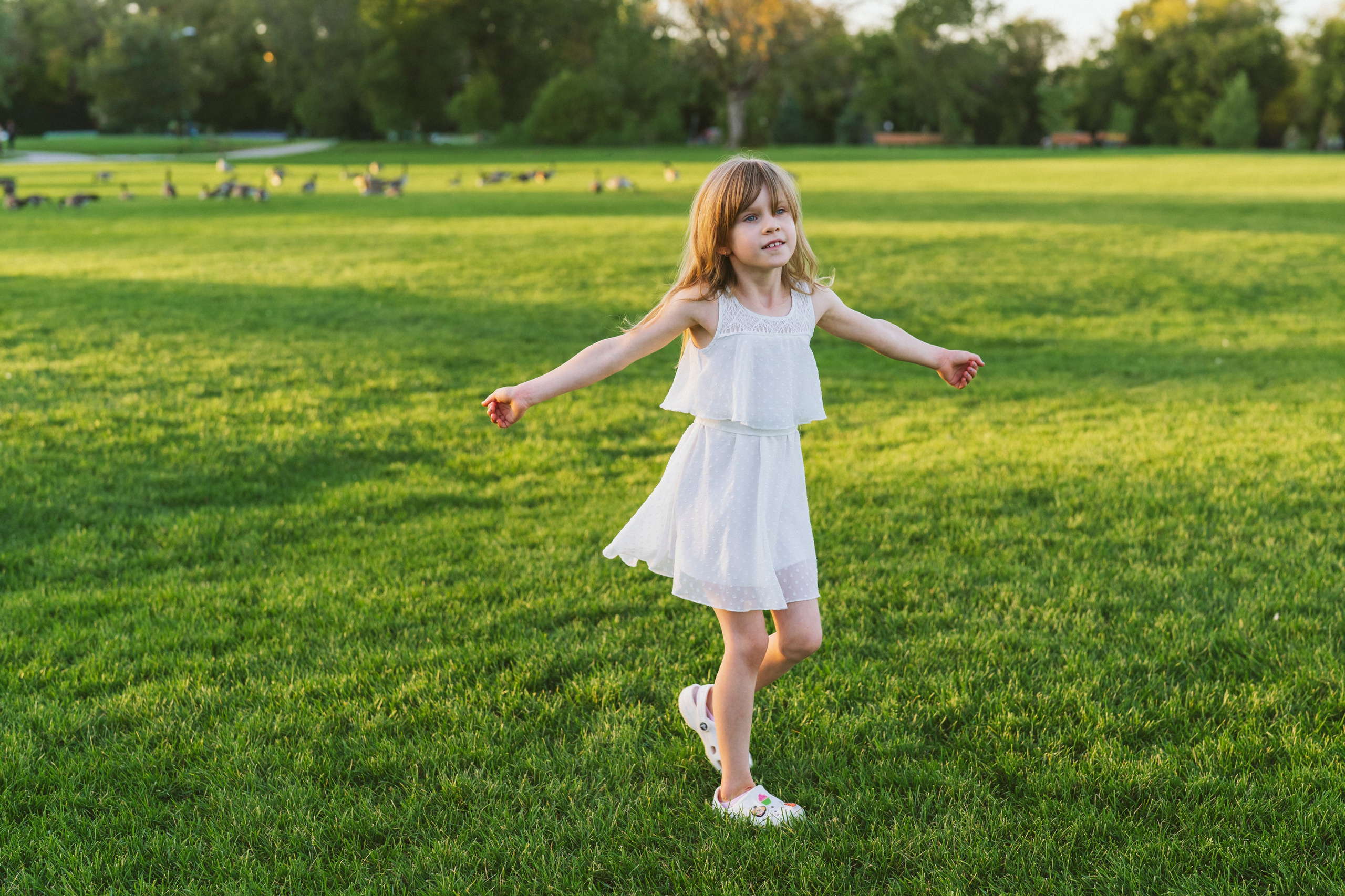 Little girl in a white dress spinning in the park