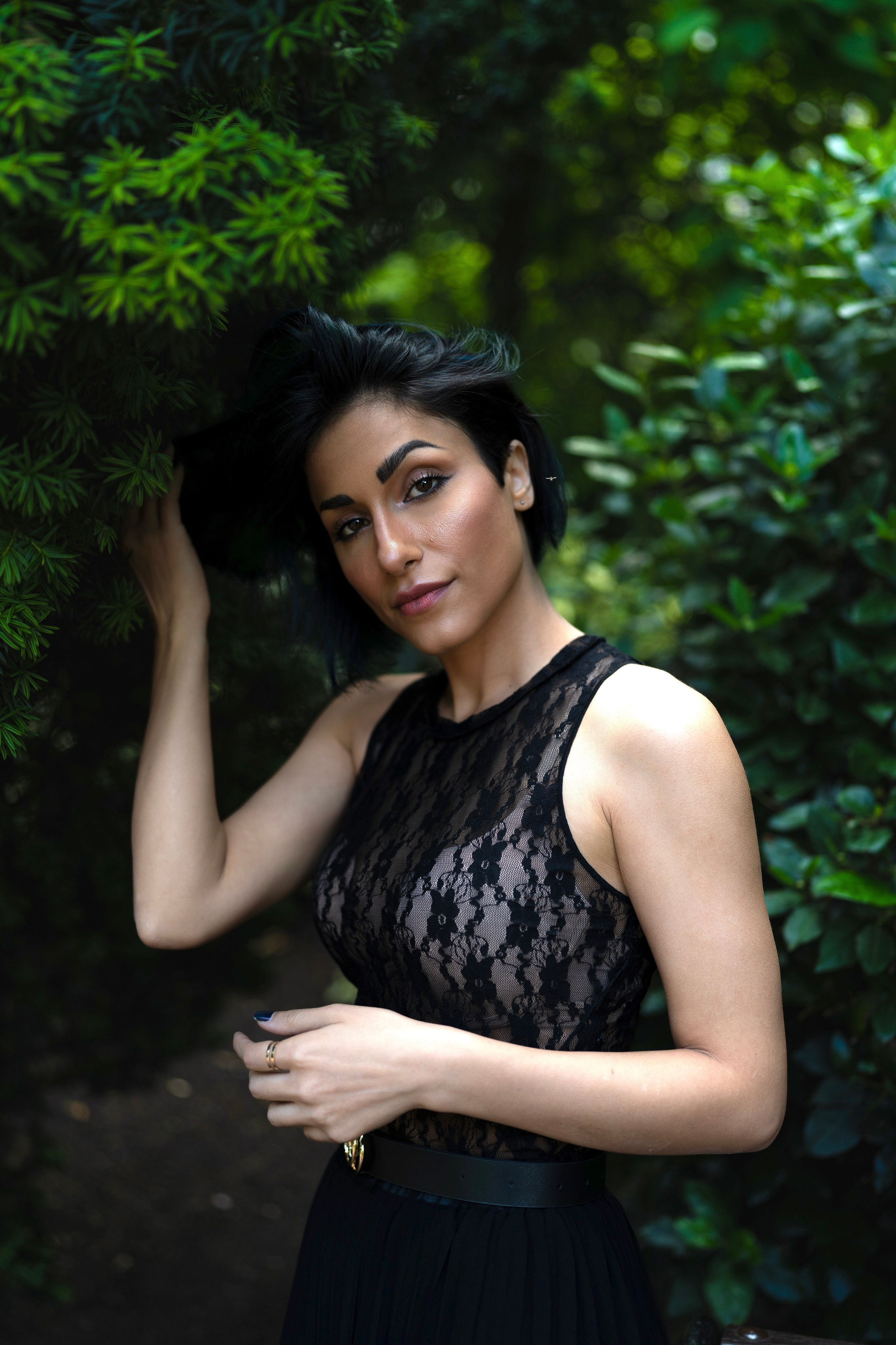 Environmental portrait of a woman framed by foliage, photographed in low natural light with a refined editorial mood.