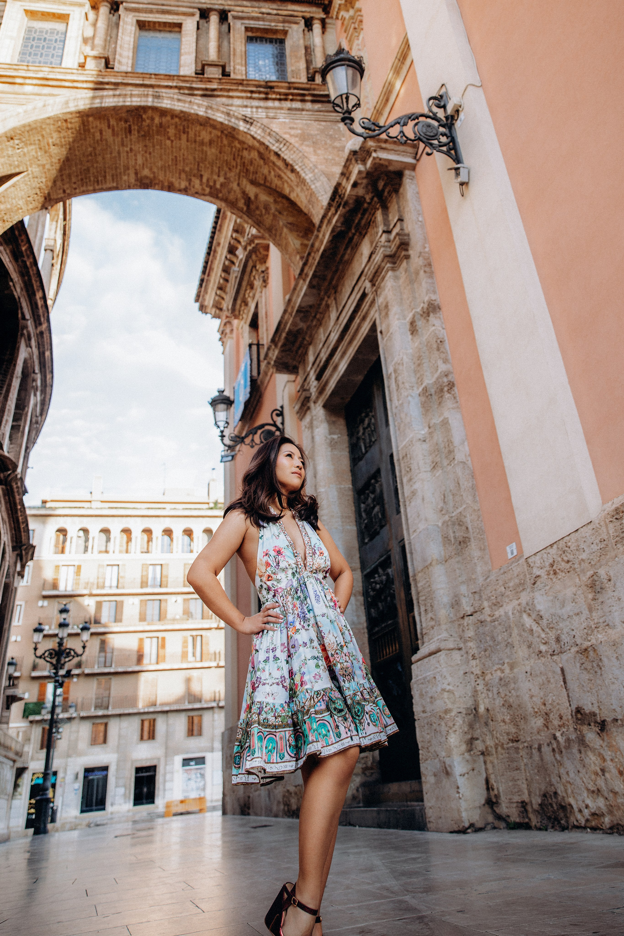 Sesión de retrato femenino en Valencia, España, con una mujer posando bajo un histórico arco de piedra en el casco antiguo. Capturada con luz natural y elegante arquitectura mediterránea de fondo para crear un retrato estilizado, seguro y atemporal, ideal para fotografía de retrato femenino, sesiones de viaje en solitario, fotografía lifestyle y marca personal en Valencia y toda España.
