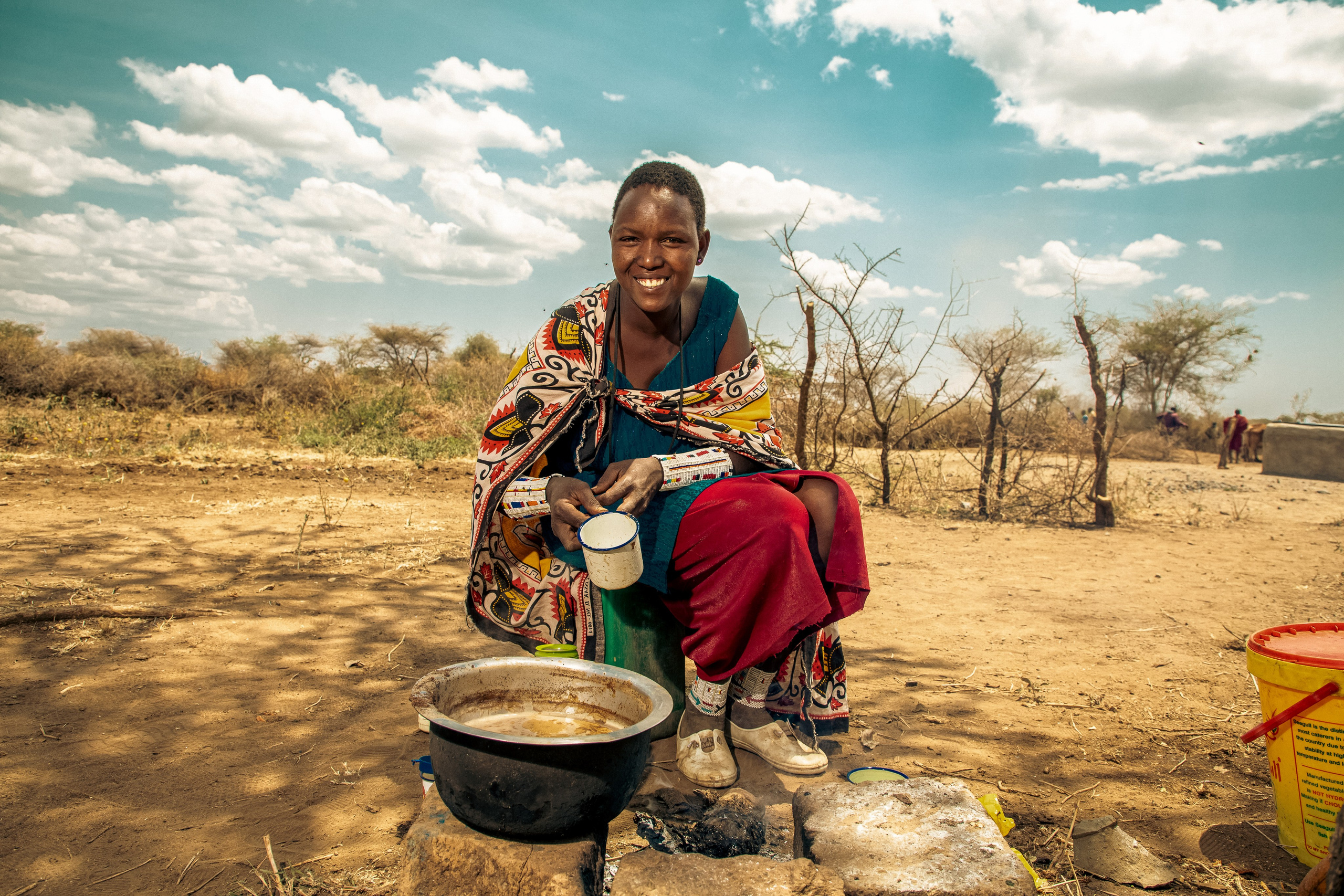 A Maasai woman, sitting on a rock, serves tea from a sufuria, at Oloomaiyana in Kajiado county. Documentary photography