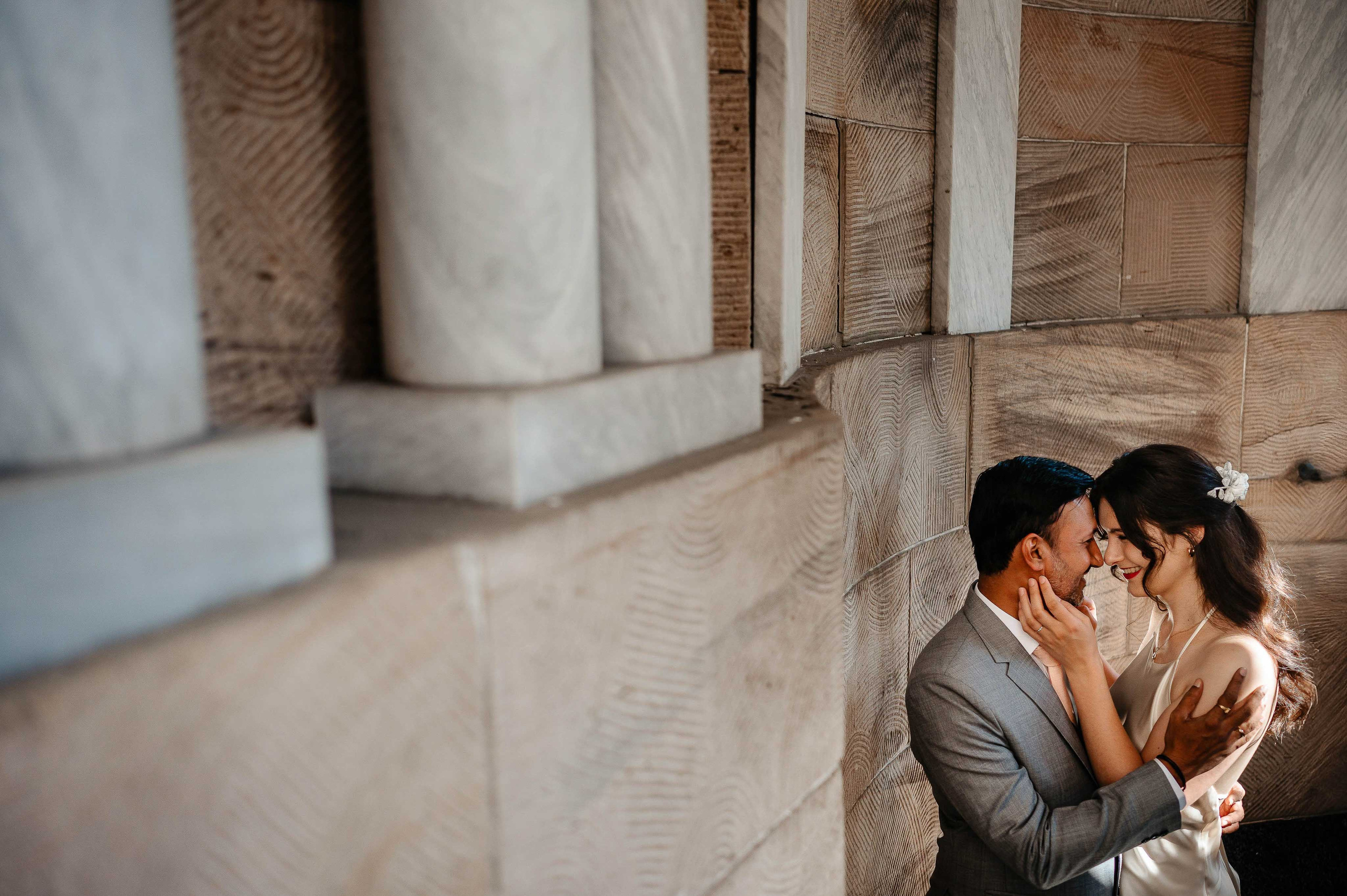 Brautpaar intime Umarmung vor Marmorsäulen, zeitlose Hochzeitsfotografie.