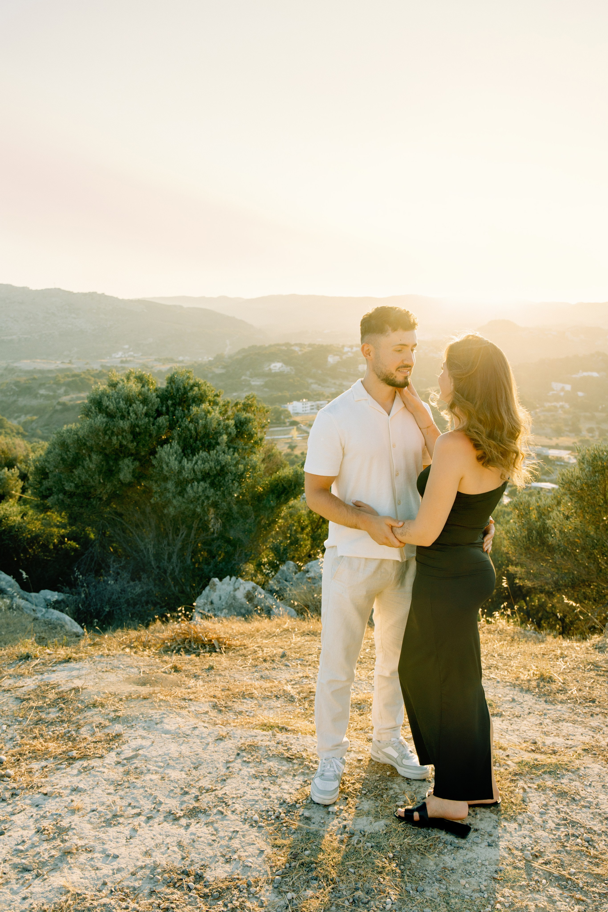 "Liebevoller Blickkontakt: Ein Paar auf dem Felsplateau des Profitis Ilias vor der Kulisse von Faliraki und dem Mittelmeer."