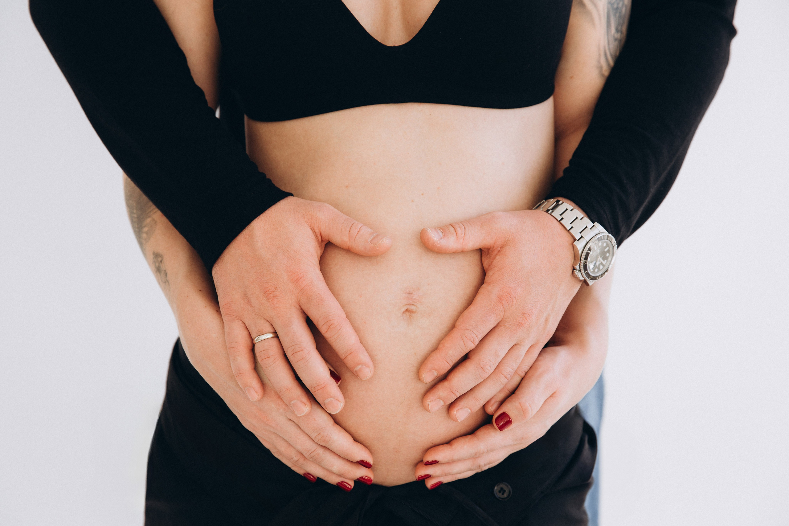 Primer plano de maternidad de una pareja abrazando con ternura el vientre de embarazo, con las manos entrelazadas simbolizando unión, amor y anticipación — capturado en un estudio luminoso en Valencia, España.
