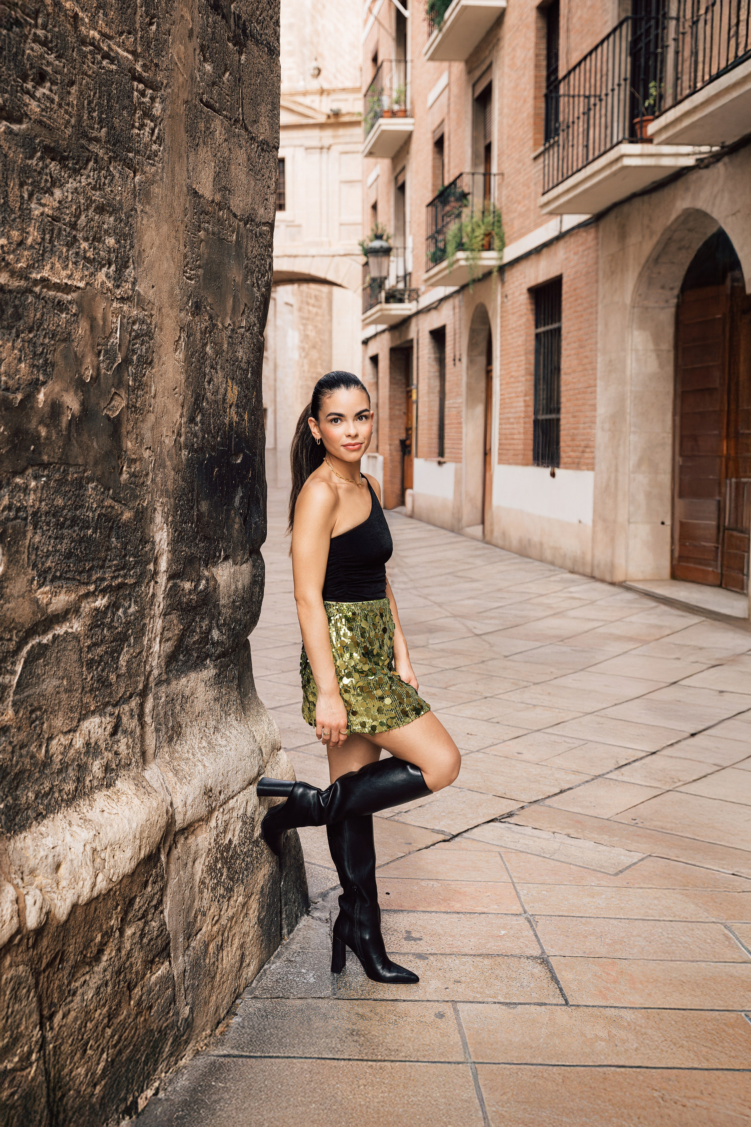 Шикарная женская портретная фотосессия на исторических улицах Валенсии, Испания — уверенная женщина в черном топе, юбке с узором и сапогах до колен. Идеально для демонстрации современной и модной женской портретной фотографии в Валенсии и по всей Испании.