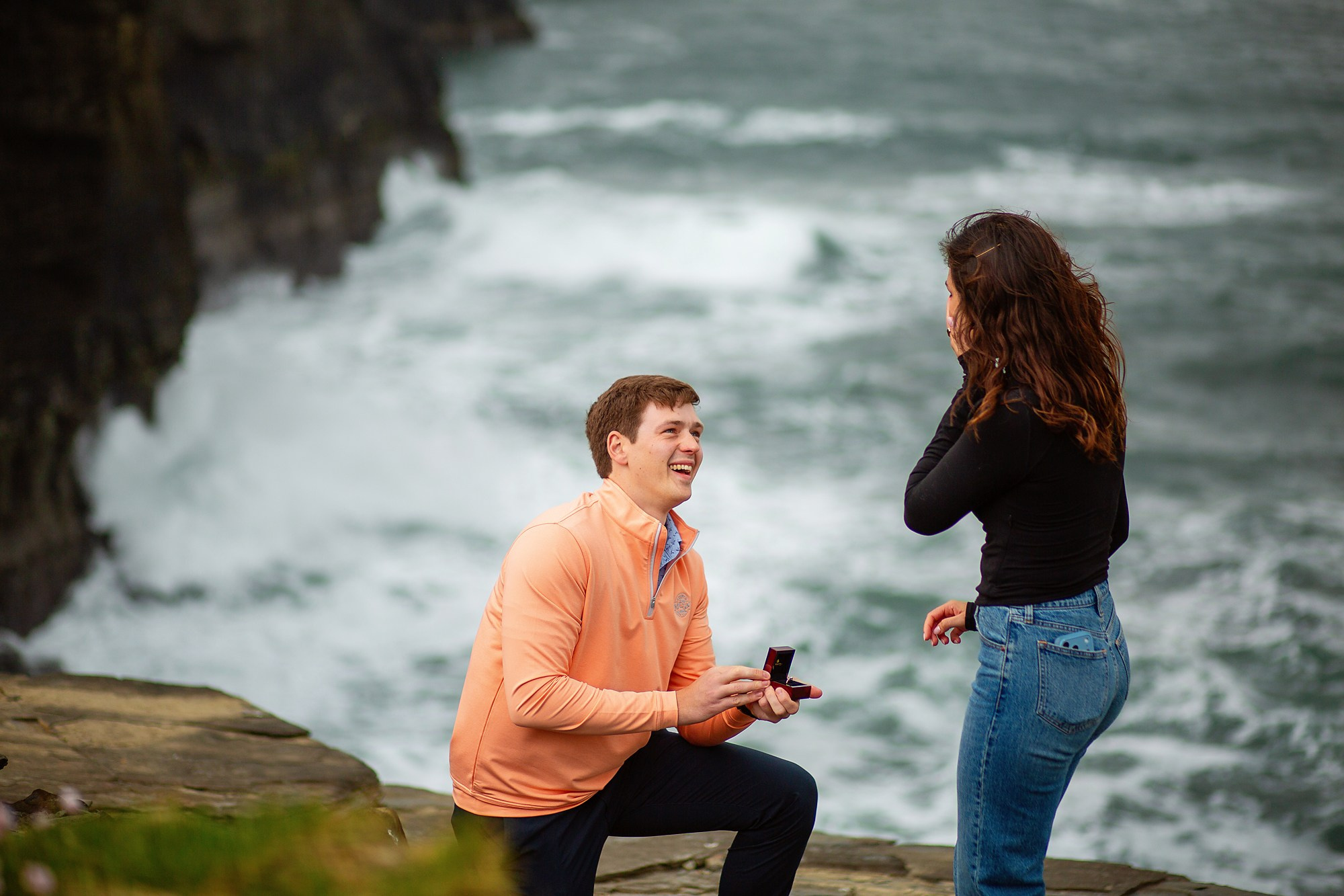 A man kneeling to propose to his partner on the rugged cliffs of Doolin, Ireland.