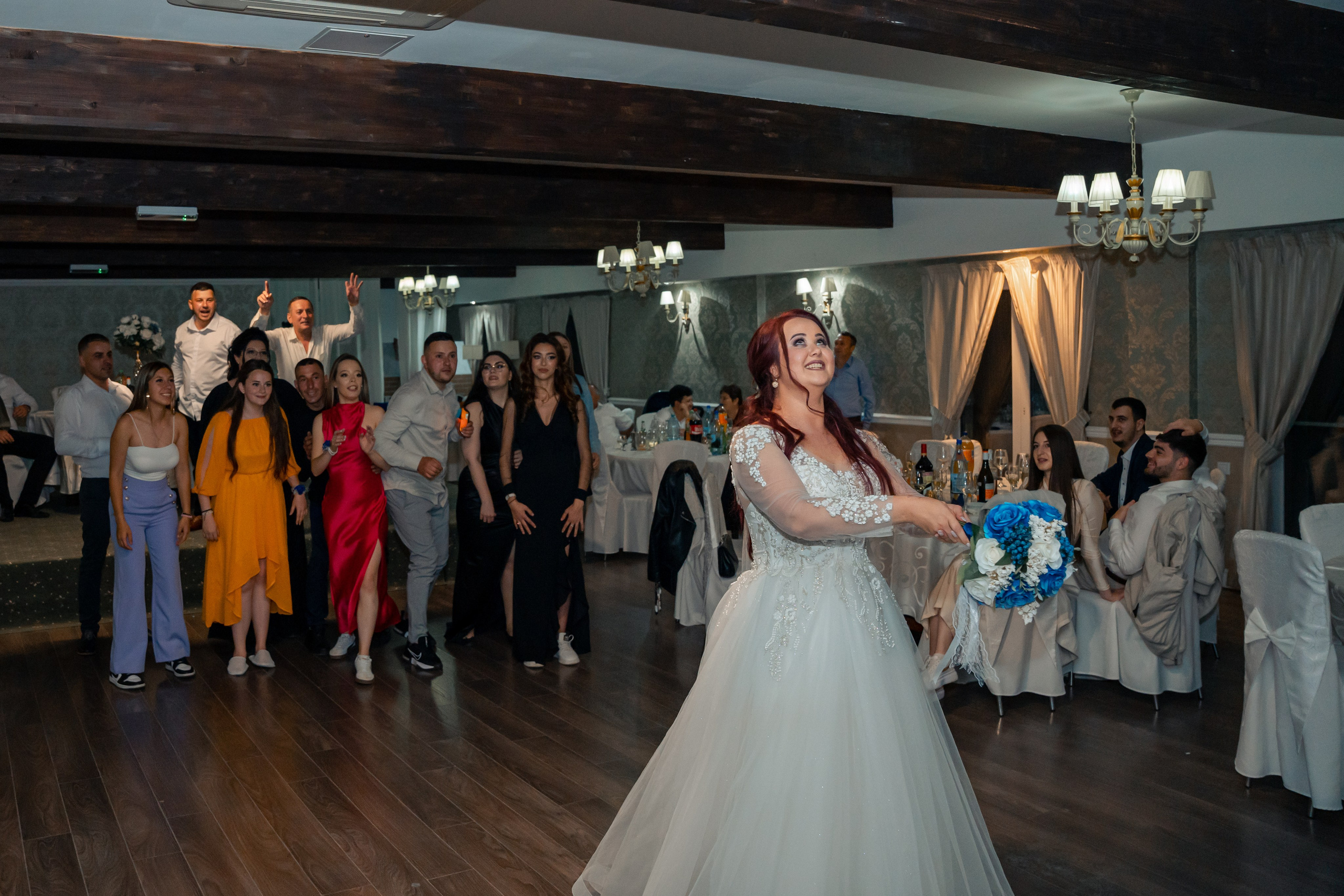 Mireasă aruncând buchetul la petrecerea de nuntă, invitați surprinși în moment dinamic, fotograf evenimente București, incadru.ro.
