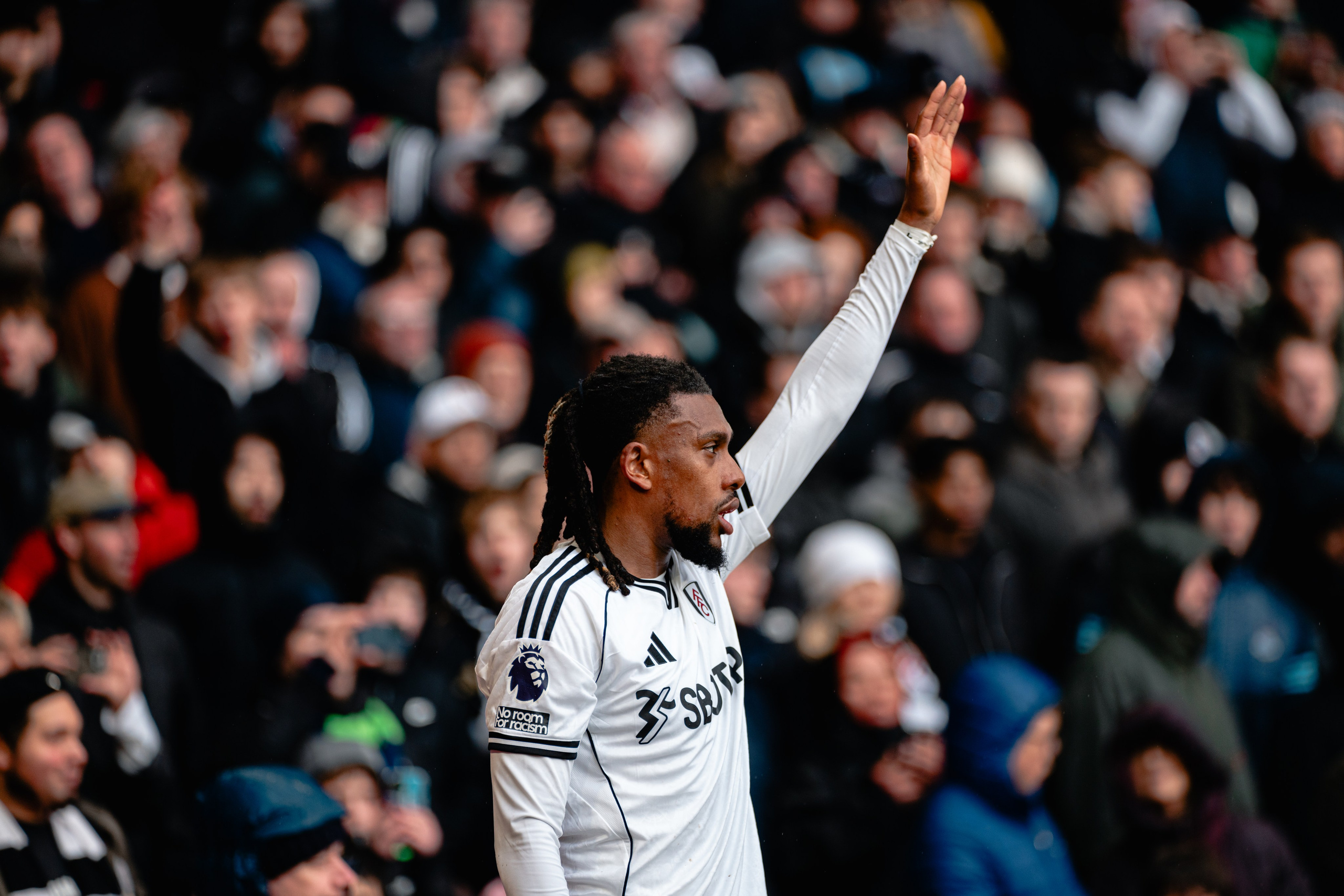 Fulham player raising an arm towards supporters during a professional football match.