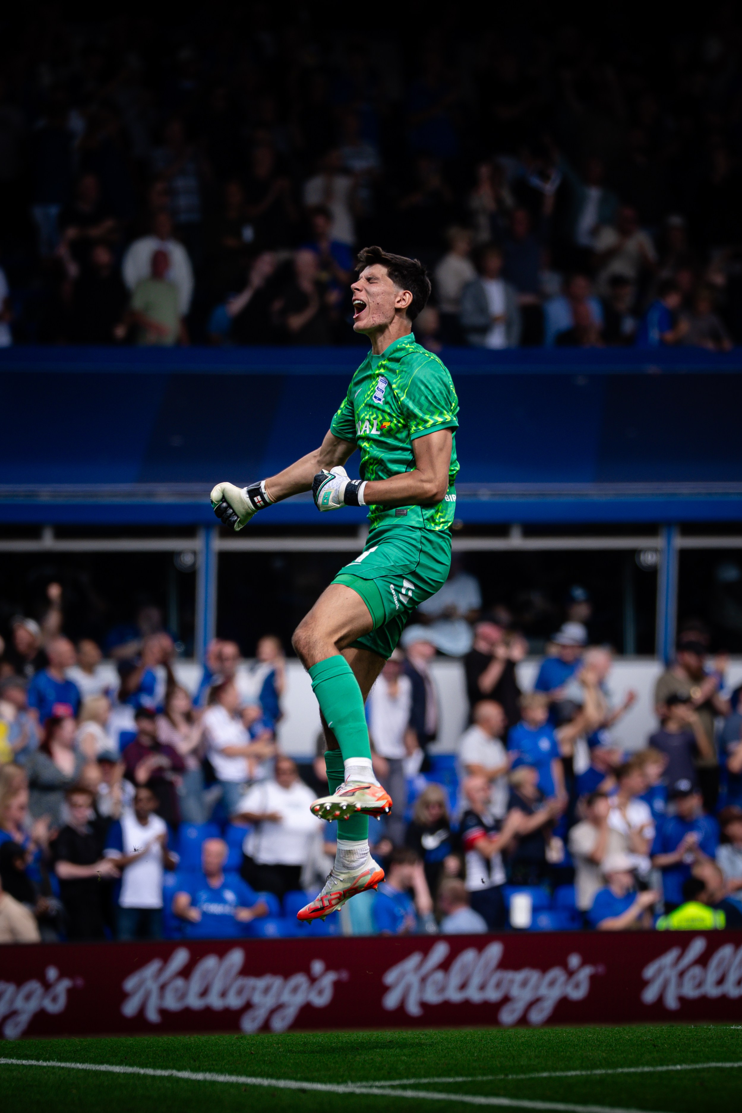 Goalkeeper jumping in celebration in front of supporters during a professional football match.