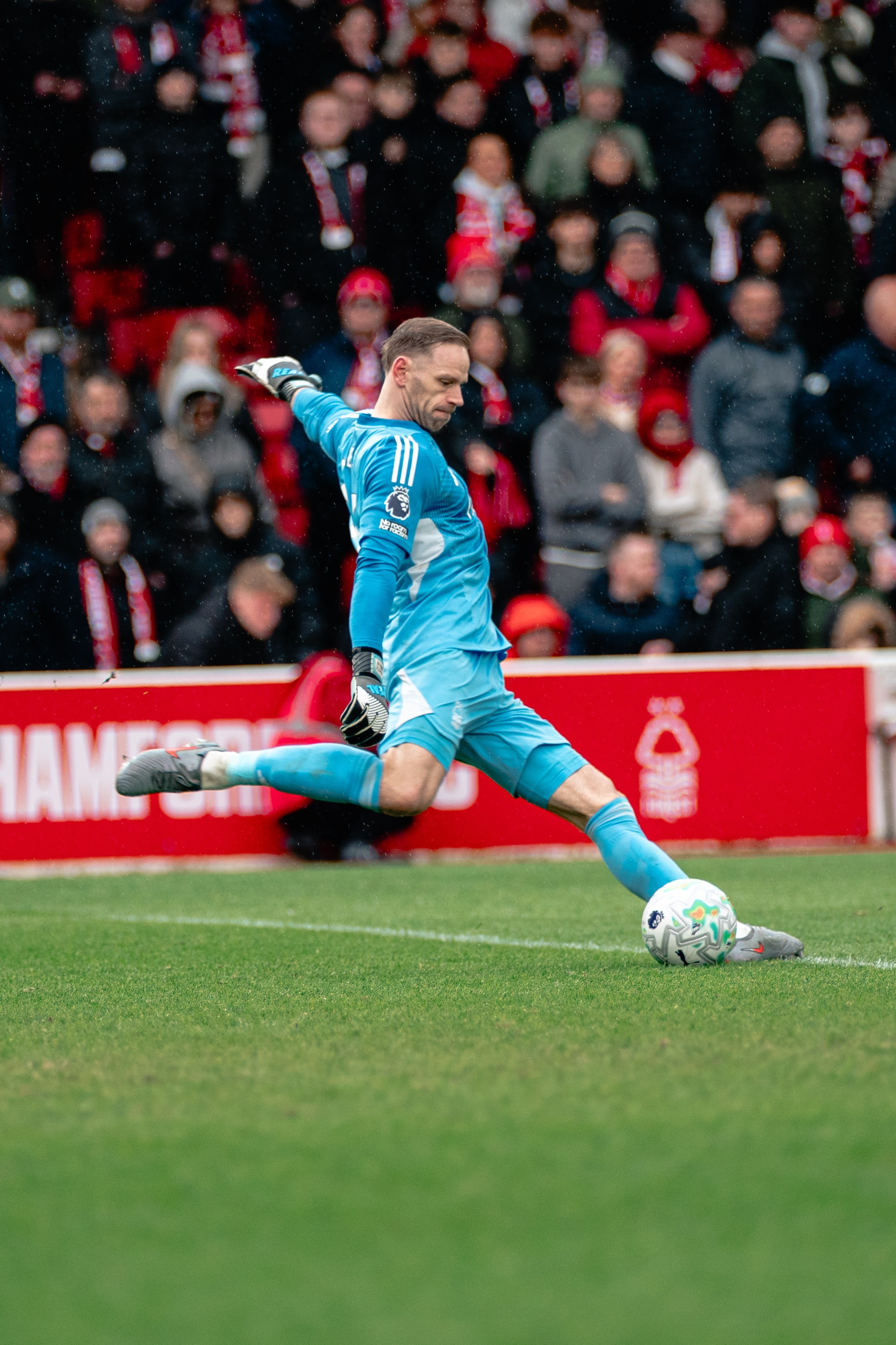 Football player in a turquoise kit striking the ball during a professional match.