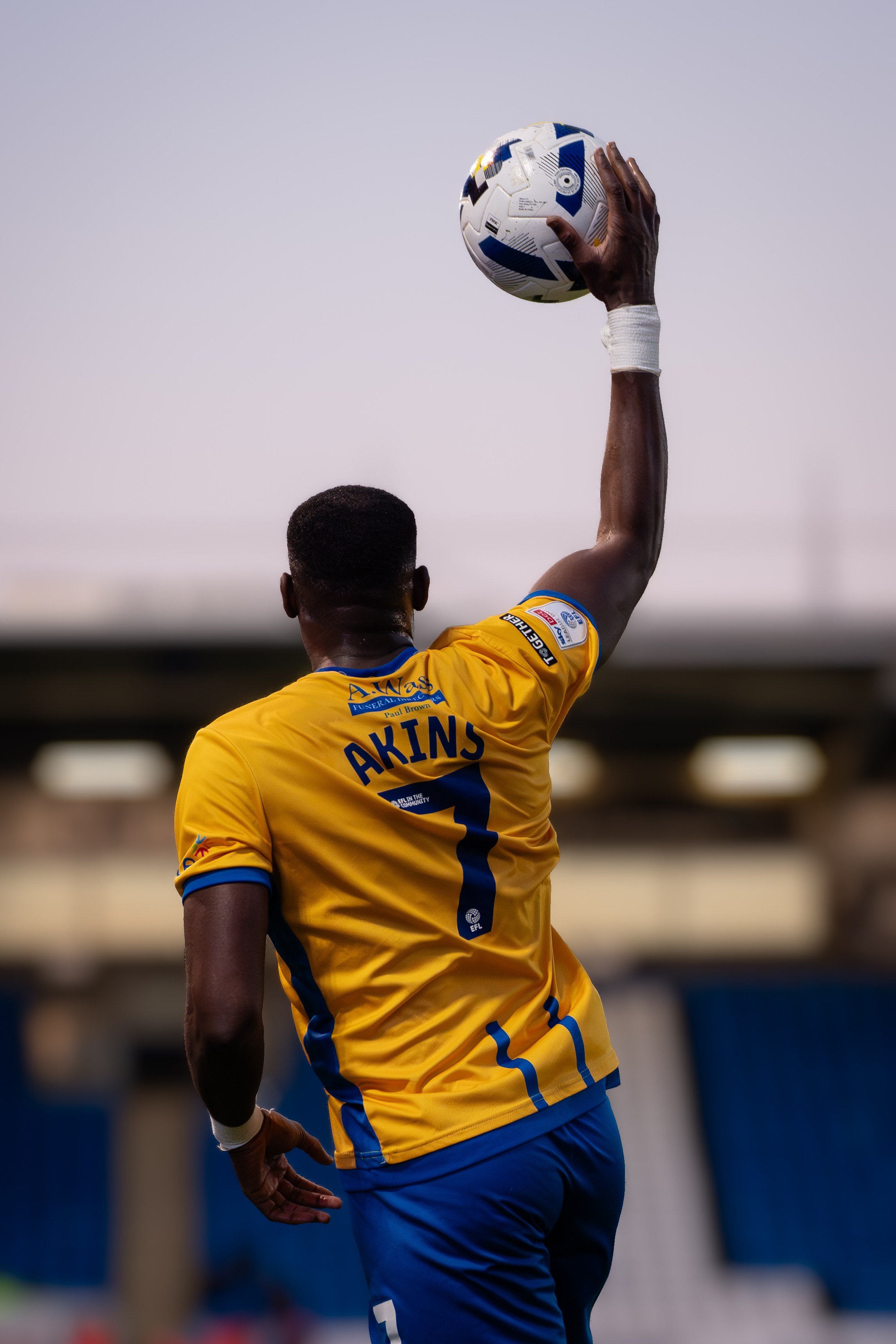 Football player in a yellow and black kit taking a throw-in during a professional match.
