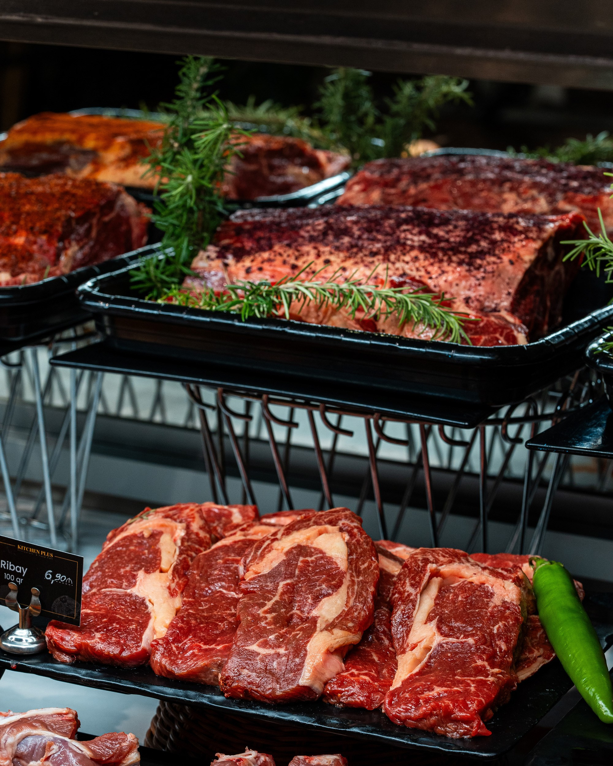 İki səviyyəli stenddə Ribeye steyk dilimləri və iri mal əti parçaları (ehtimal ki, New York kəsimi), yaşıl bibər və rozmarin qarnituru ilə.