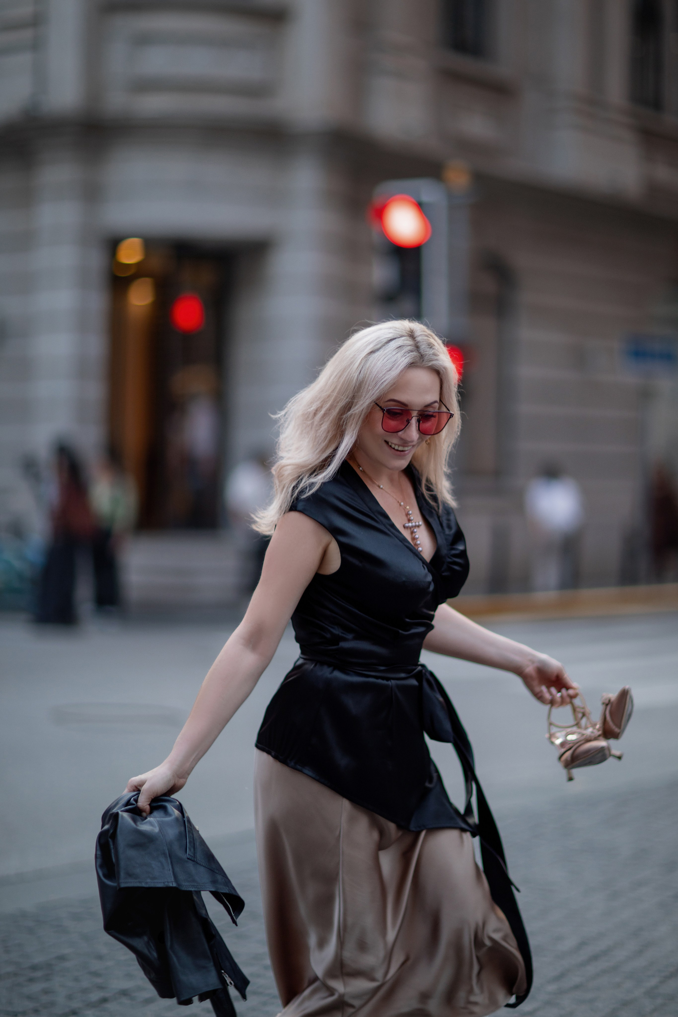 Walking photo shoot in Shanghai. Blonde girl takes off her shoes and runs barefoot on the streets of the city, holding her shoes in her hand.