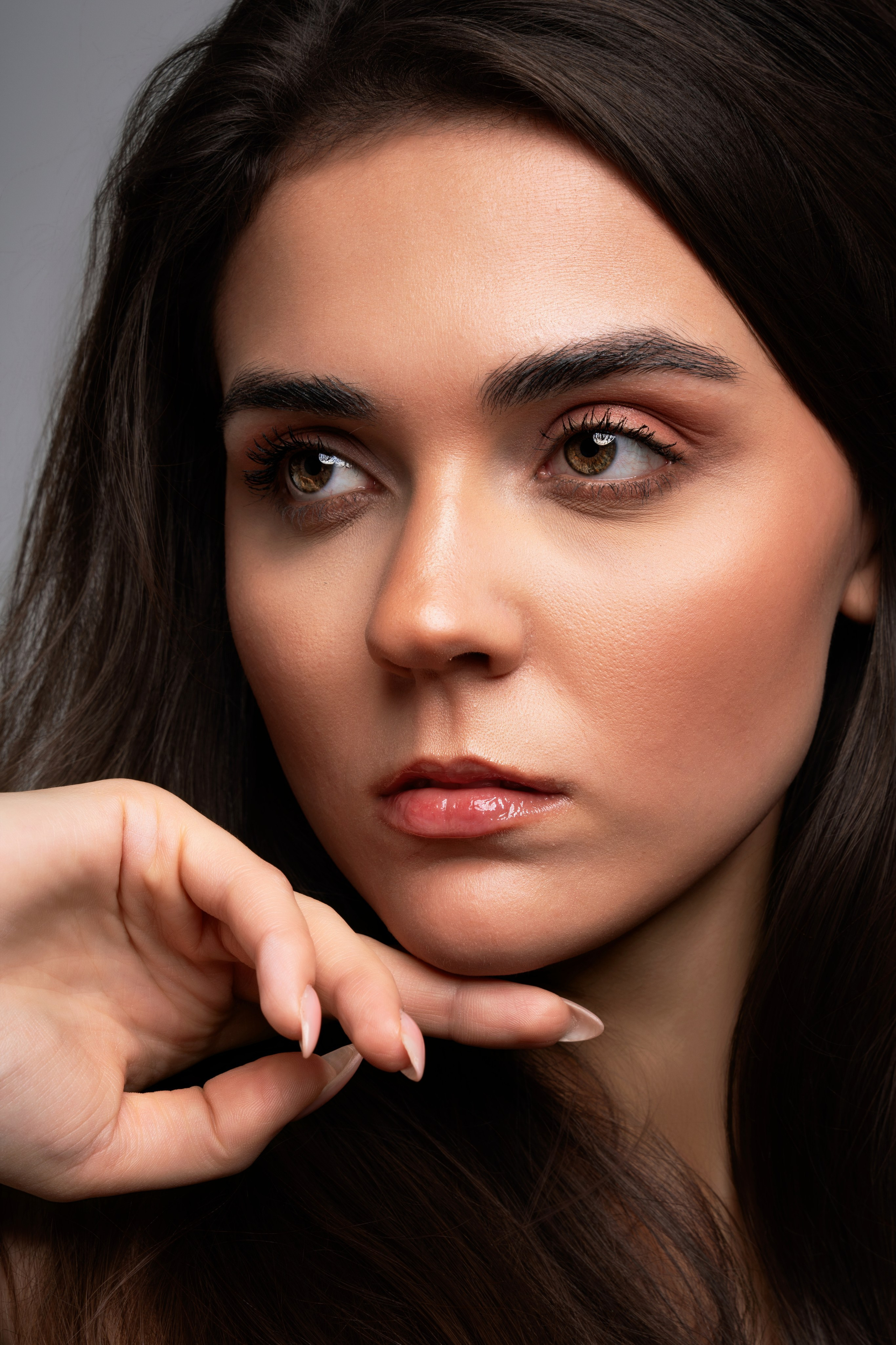 Close beauty portrait of a brunette woman with soft makeup and direct gaze, photographed in a clean editorial style.