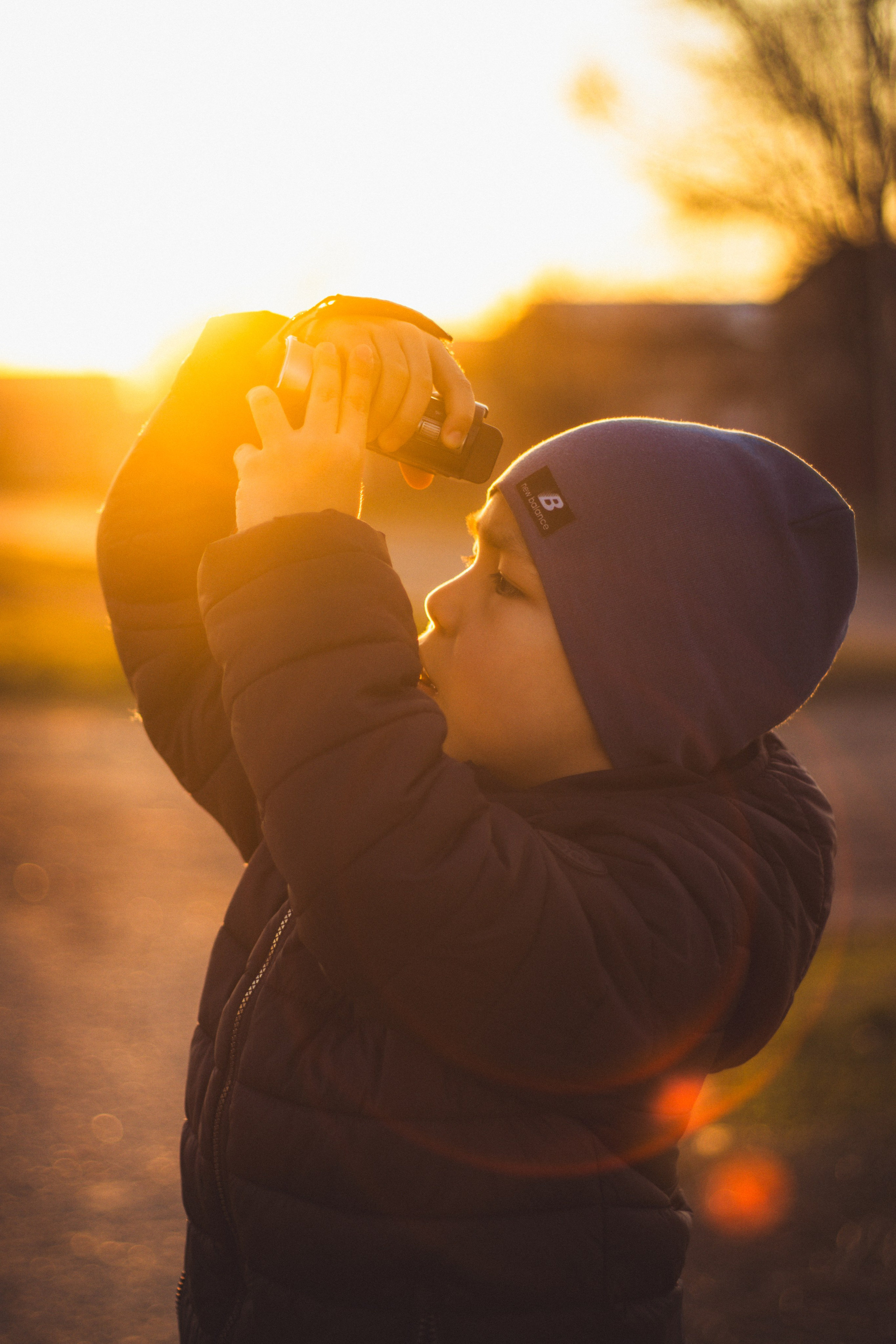 Fotografie kreativní aktivity: dítě s kamerou při západu slunce se silným podsvícením.