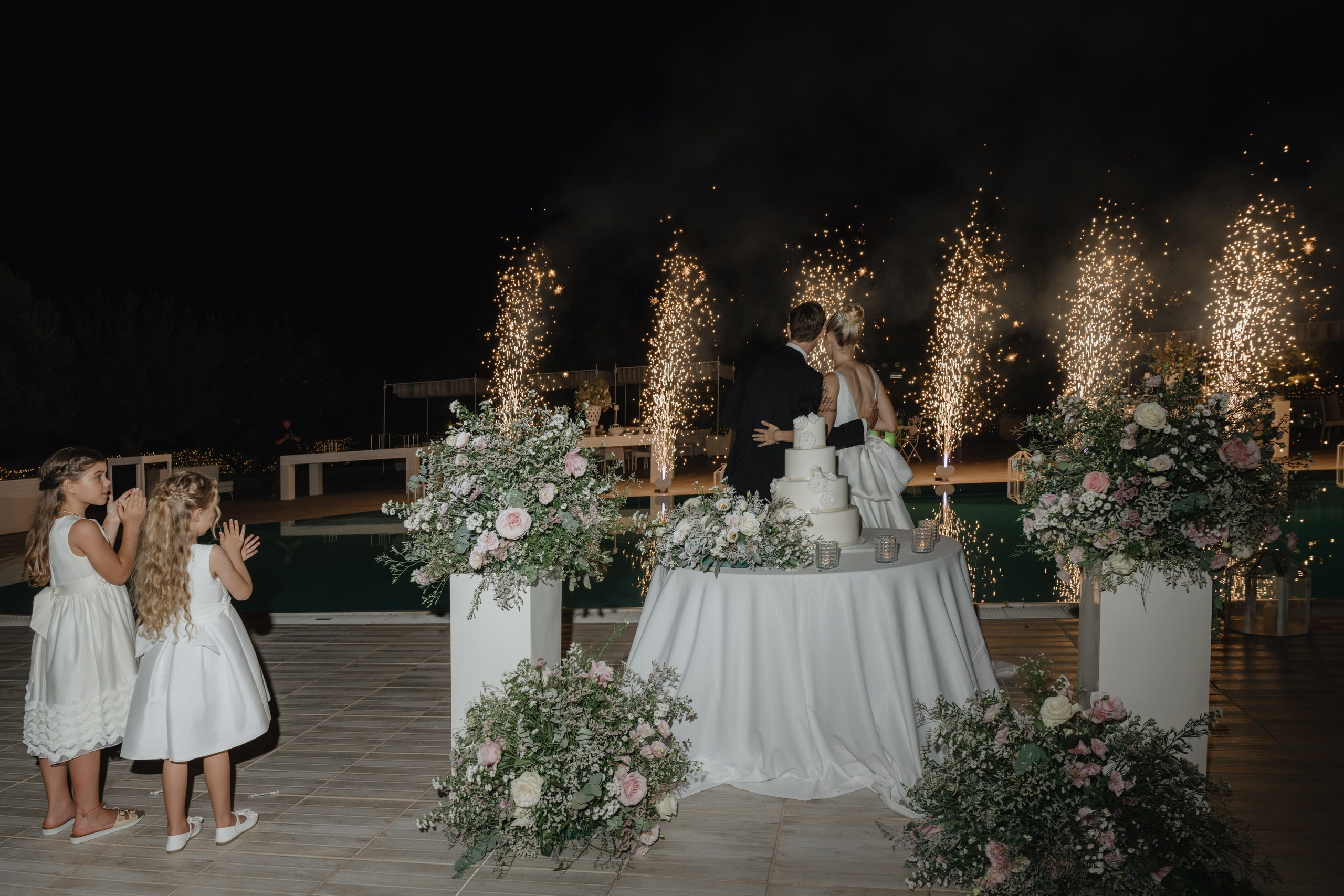 Bride and groom cutting wedding cake during reception at Masseria Traetta Ostuni with fireworks on background 