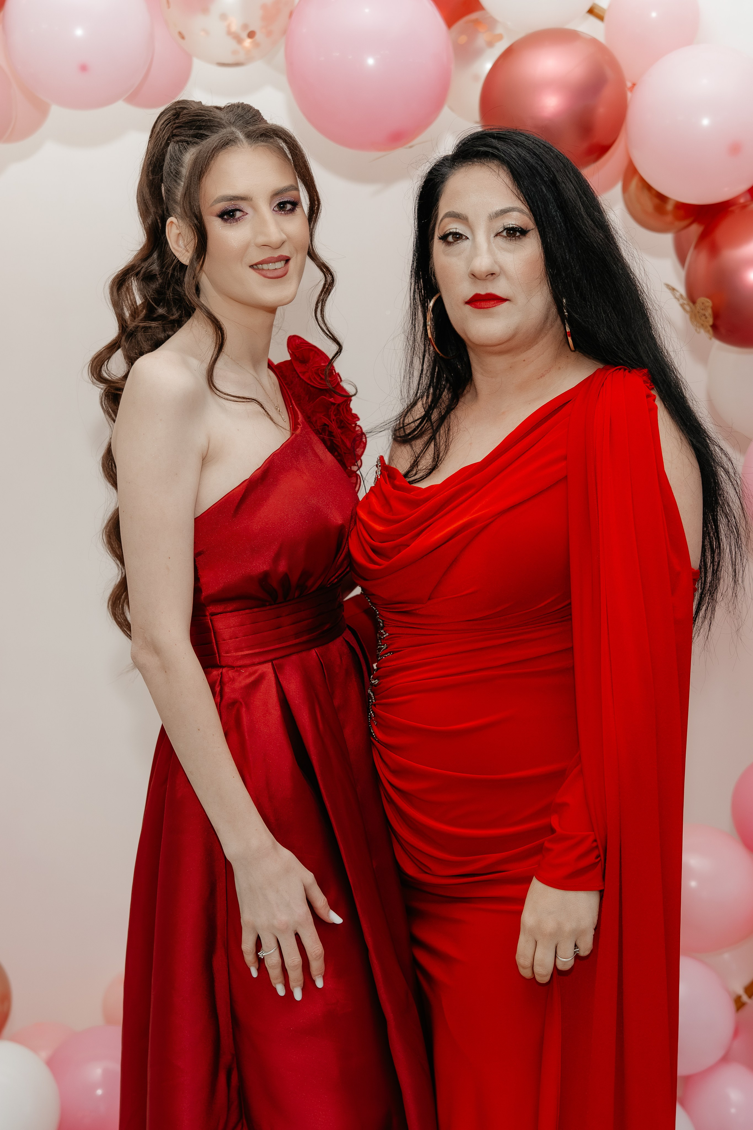 Close-up fericit la petrecerea de botez: mama Maria și nașa, îmbrăcate în roșu elegant, zâmbesc larg într-un cadru apropiat și intim la Restaurantul Silmat din Bălăbănești, Galați. Emoție și căldură autentică.