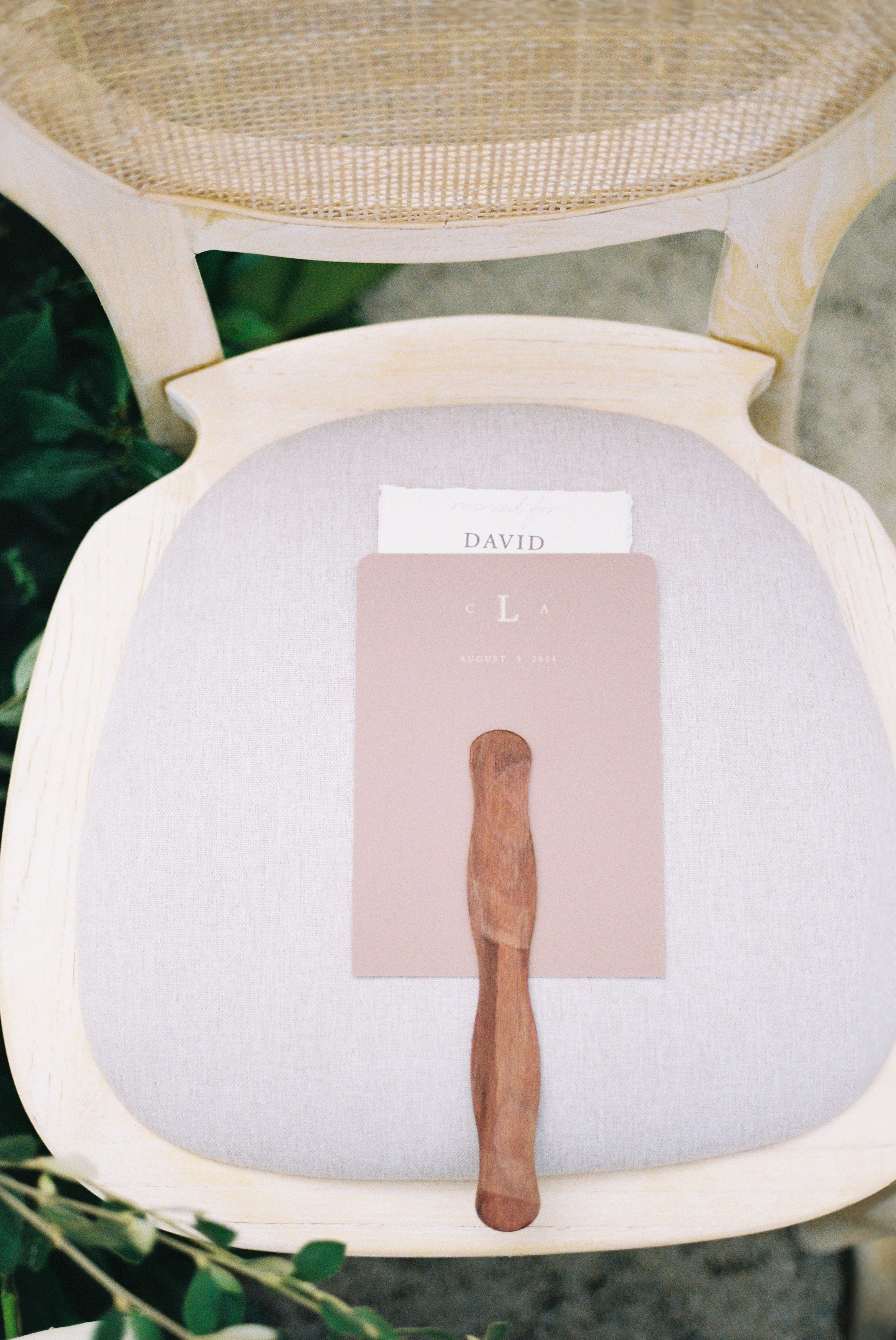 Elegant wedding program and fan placed on light-colored chair, ready for outdoor ceremony guests.