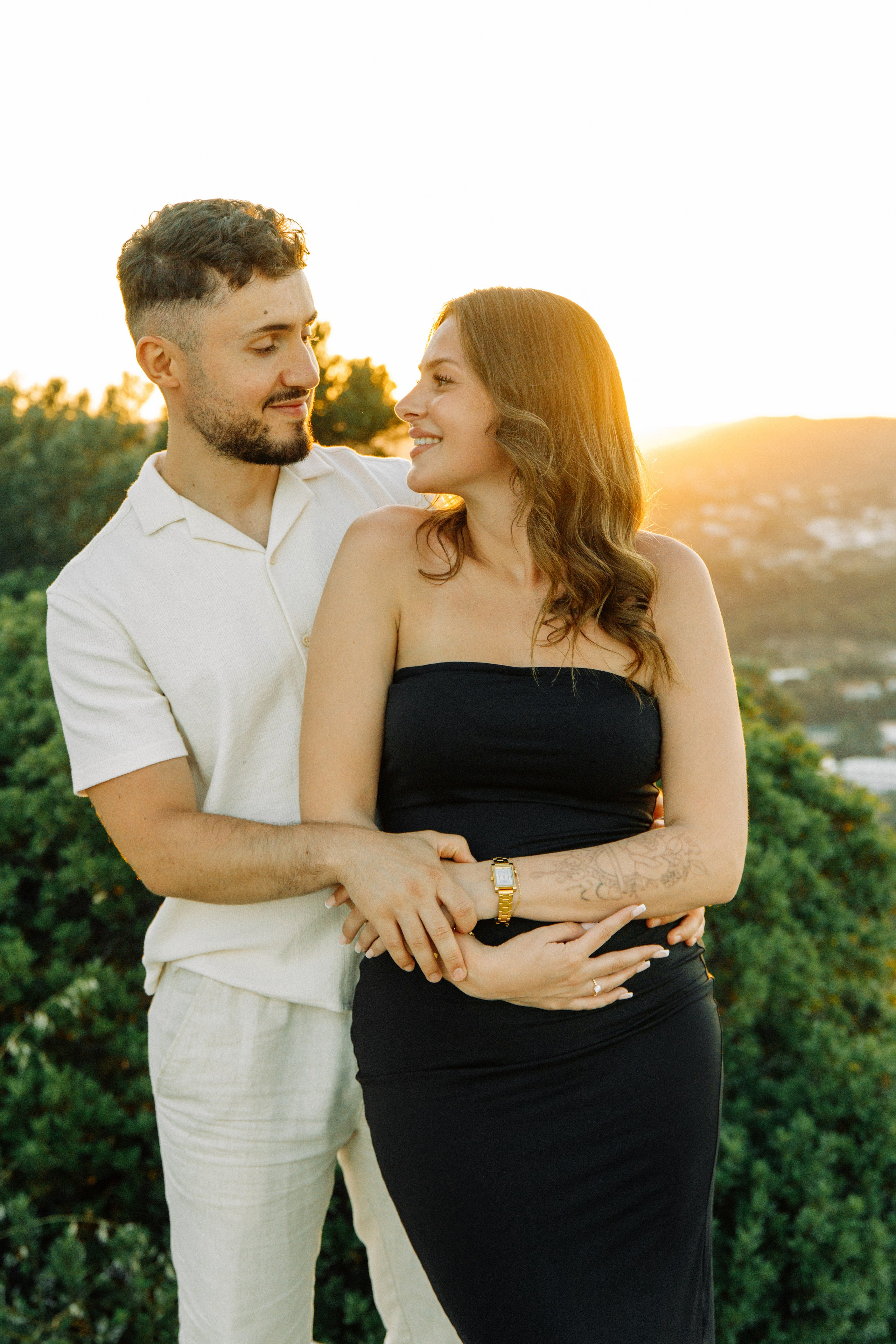 "Liebevoller Blickkontakt: Ein Paar auf dem Felsplateau des Profitis Ilias vor der Kulisse von Faliraki und dem Mittelmeer."