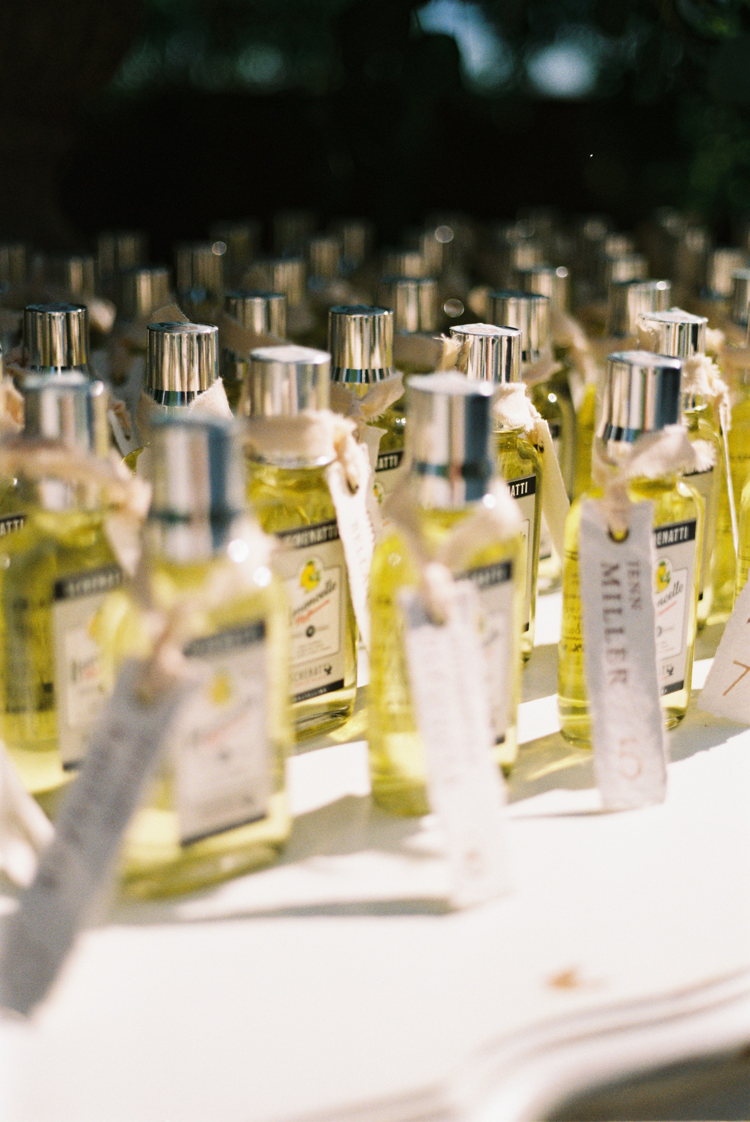 Close-up of miniature limoncello bottles with personalized tags as wedding favors on display table.