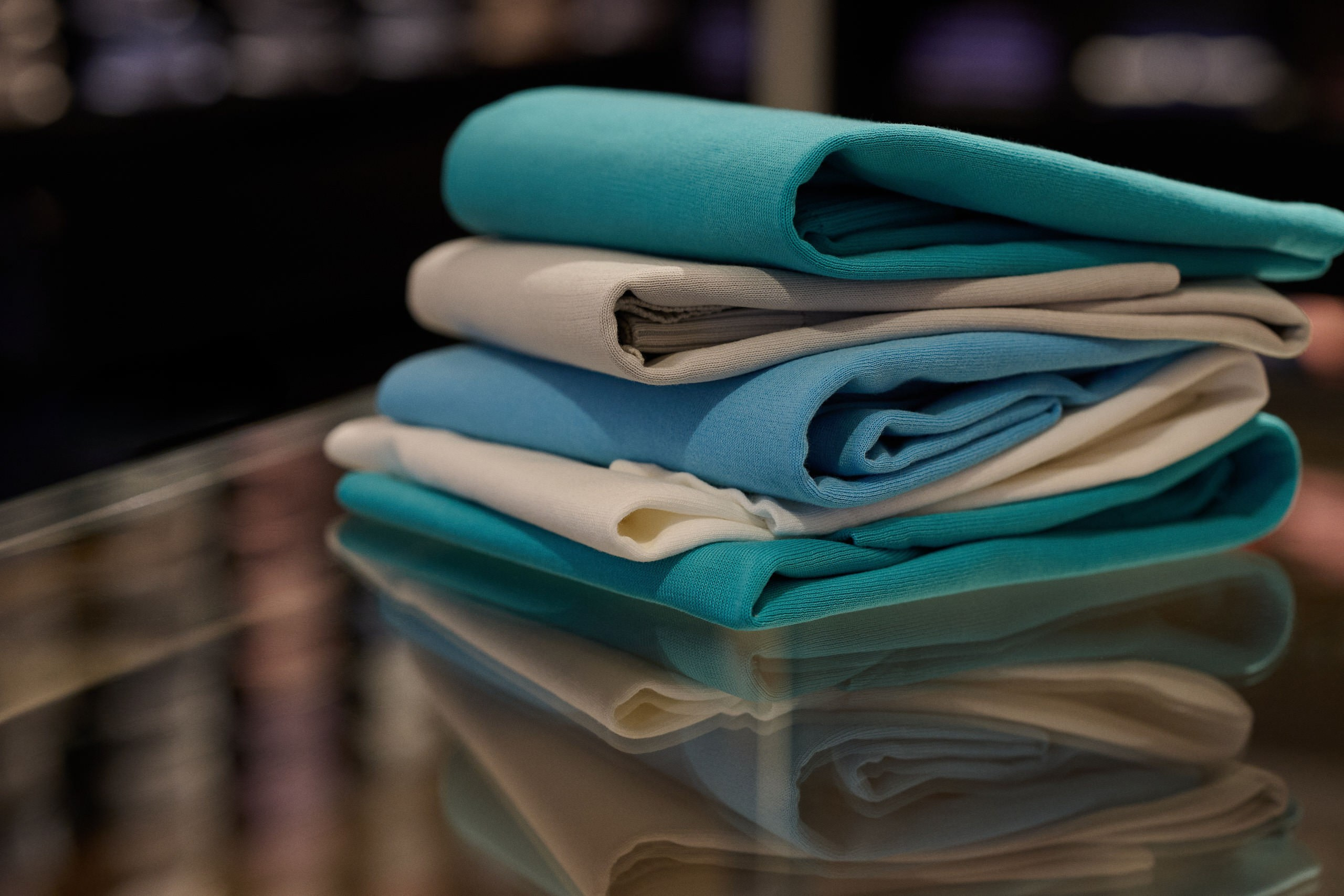 Produktfotografie Wien – Gefaltete Einstecktücher und Krawatten in Pastelltönen auf Glastisch.