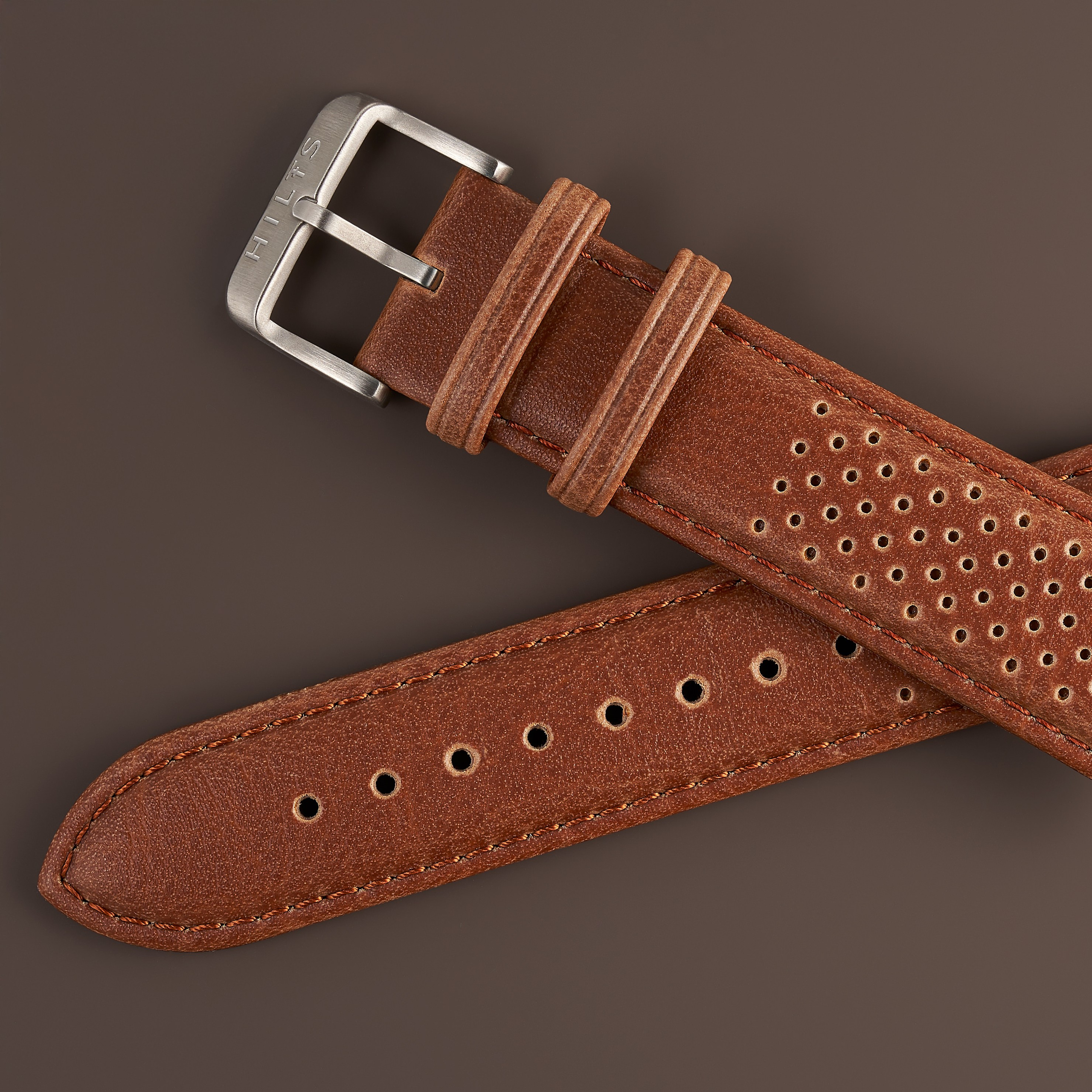 Macro detail of a perforated tan leather watch strap and steel buckle