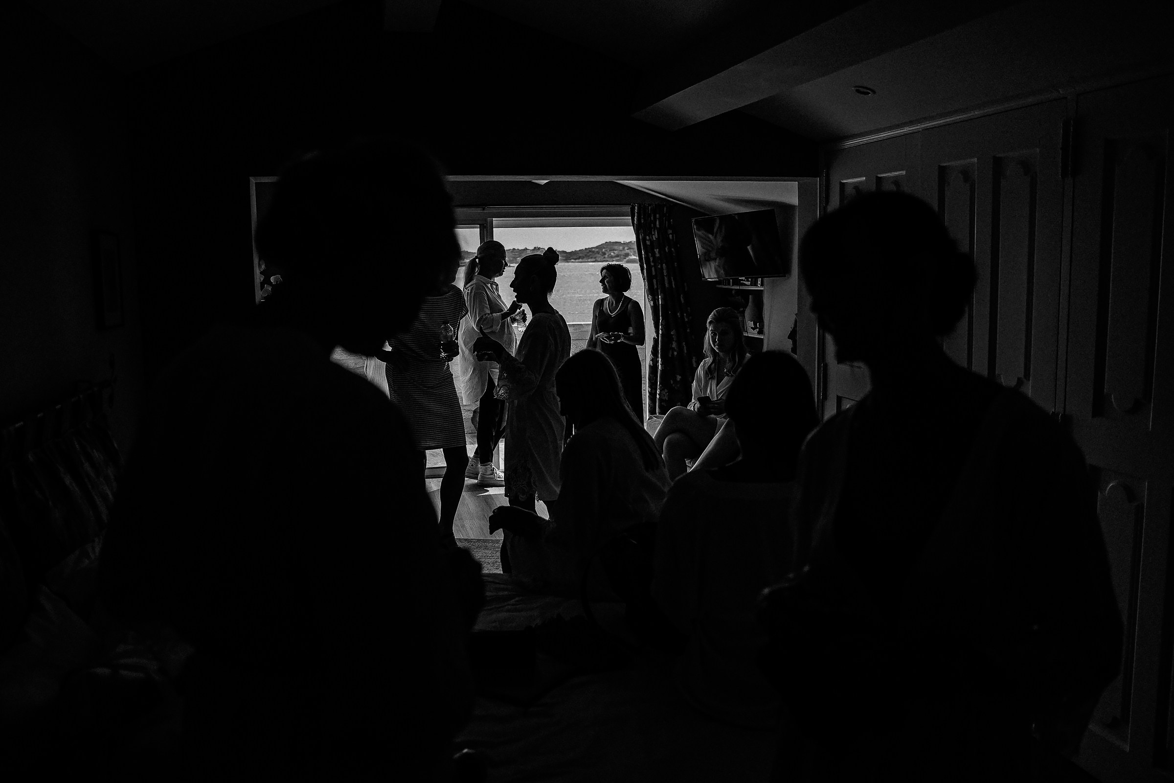 A dramatic black-and-white silhouette of bridesmaids engaging in lively conversation, with a glimpse of the beautiful Provence landscape outside.