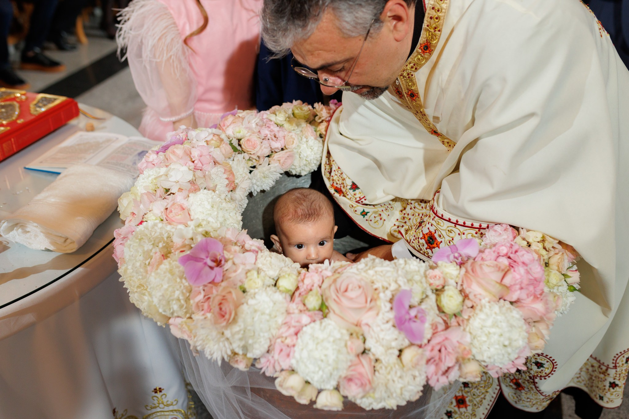Fotografie cu bebelusul scaldat in cristelnita , in timpul ceremoniei de botez.