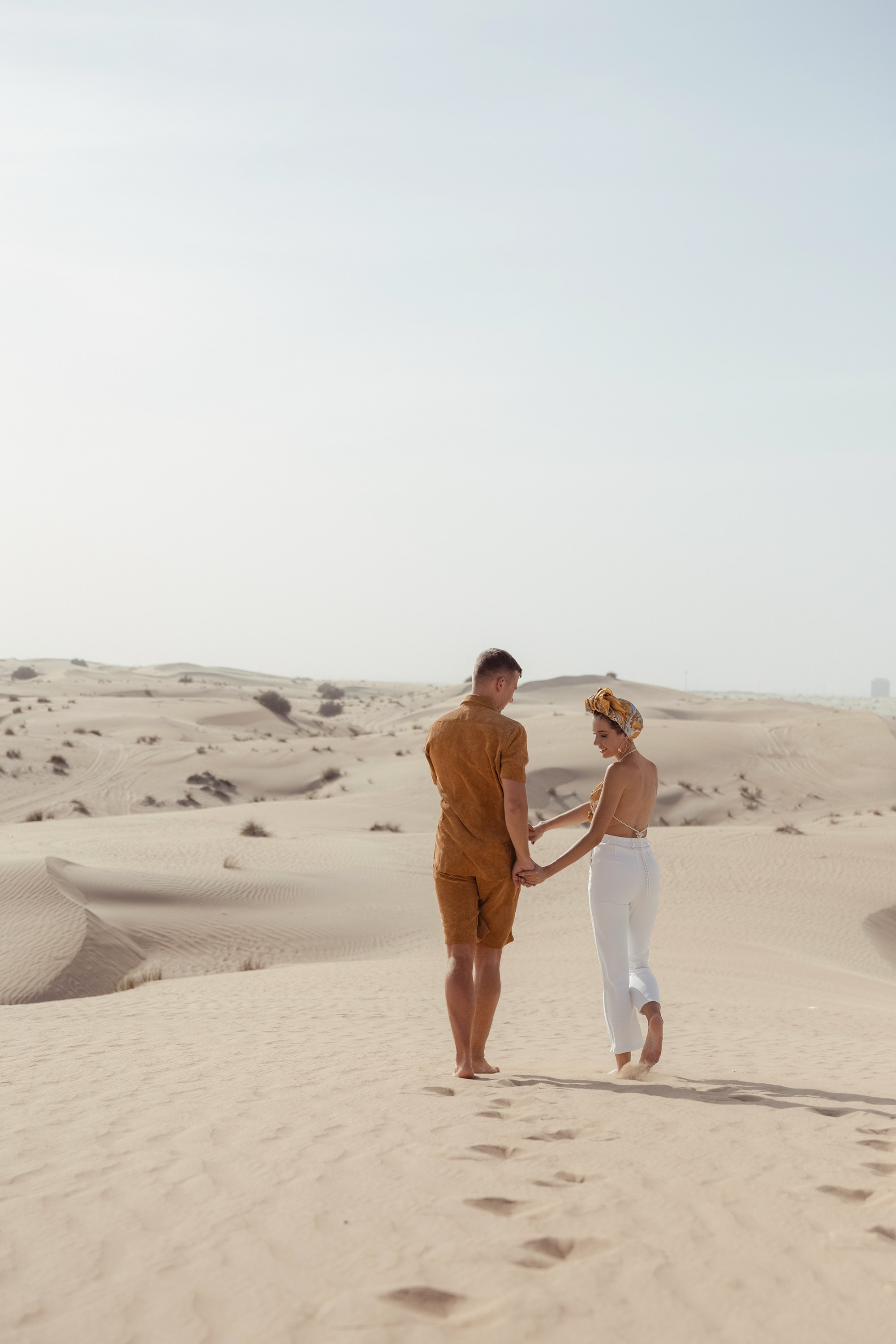 two lovers share a joyful embrace in the middle of a vast desert, surrounded by endless sand and a clear blue sky. Dubai, United Arab Emirates
