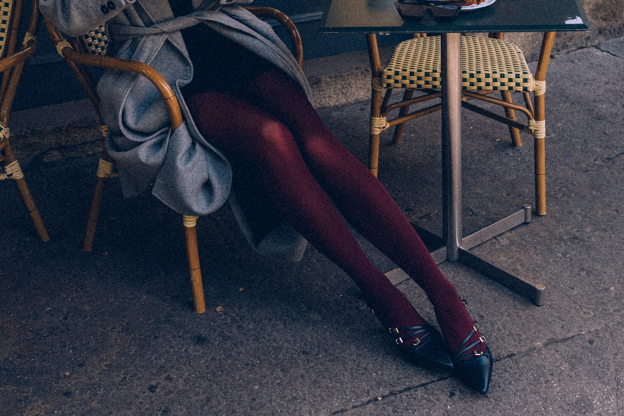 Close-up of a stylish woman's legs in burgundy tights and pointed black heels, elegantly crossed while sitting at a Milanese cafe. Milan photographer for tourists