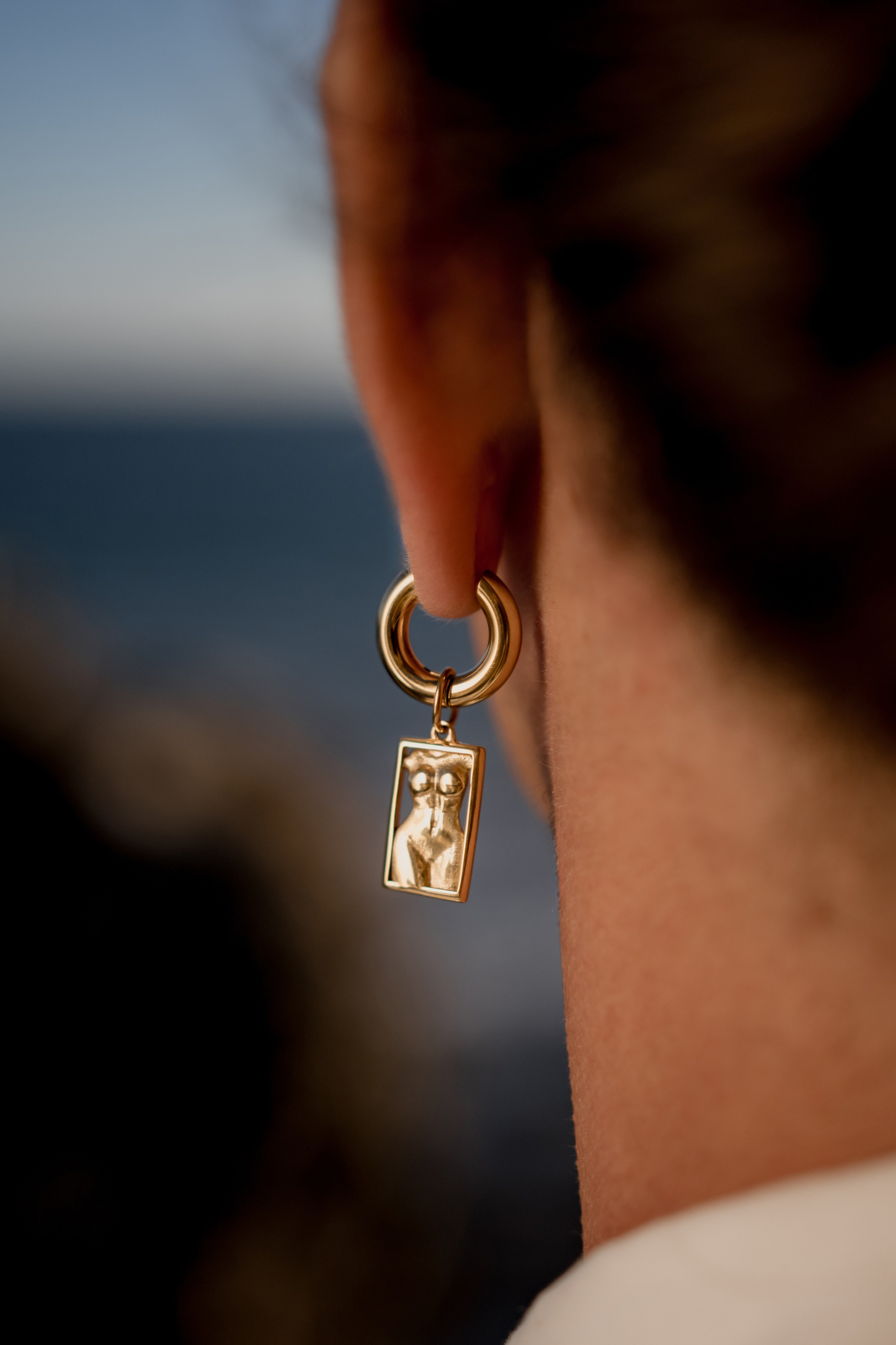 Dangling gold earrings styled in a beach setting, emphasizing coastal elegance.